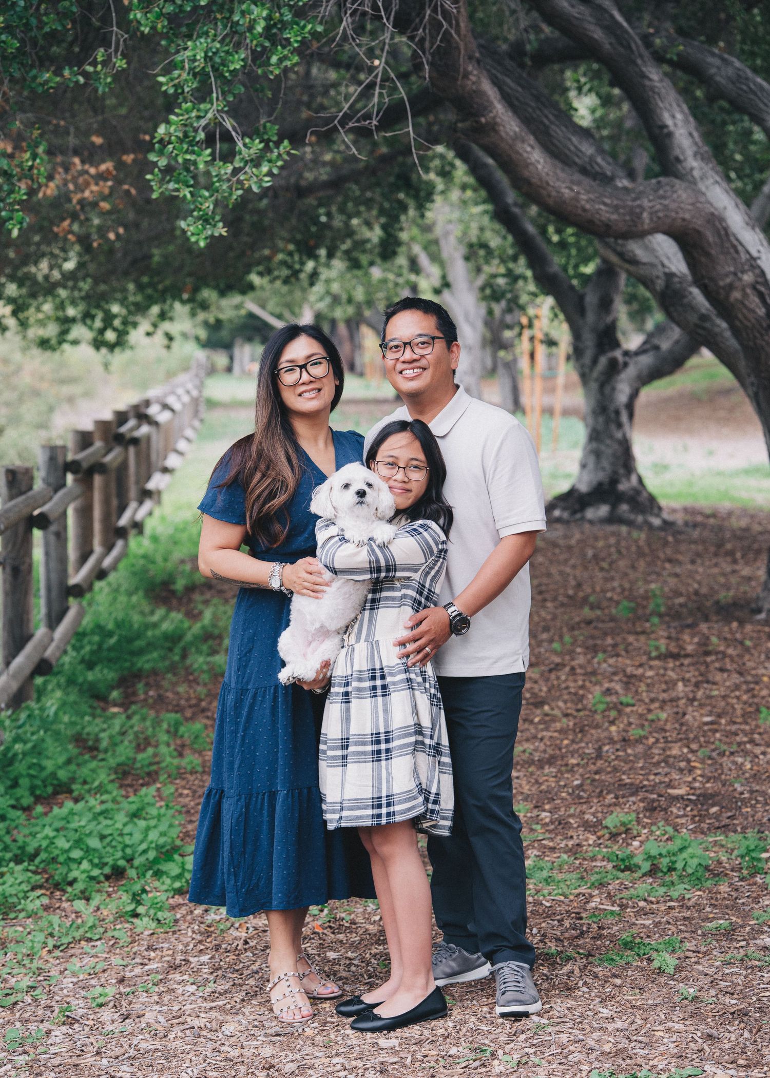 Family enjoying a playful moment together in an outdoor park setting with lush trees and fallen leaves on the ground.