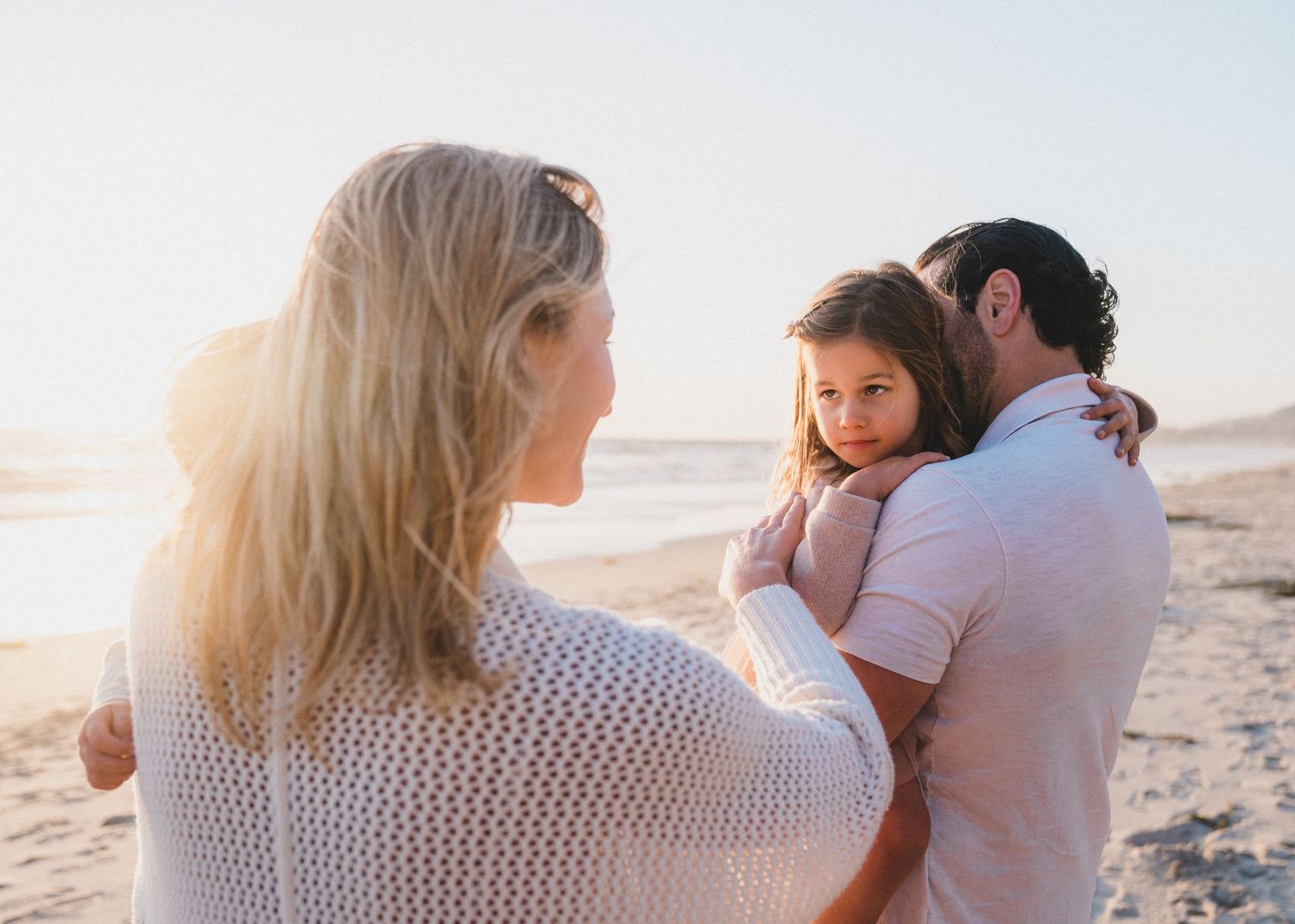 A romantic scene of people embracing on a sunlit beach during golden hour.