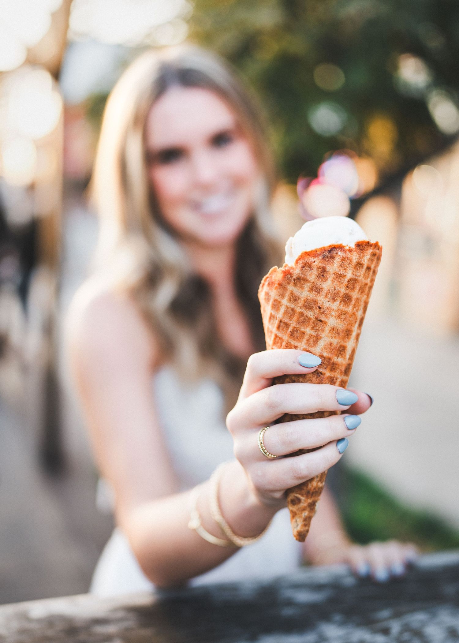 A hand holds up a crispy golden waffle against a blurred outdoor background in warm sunlight.