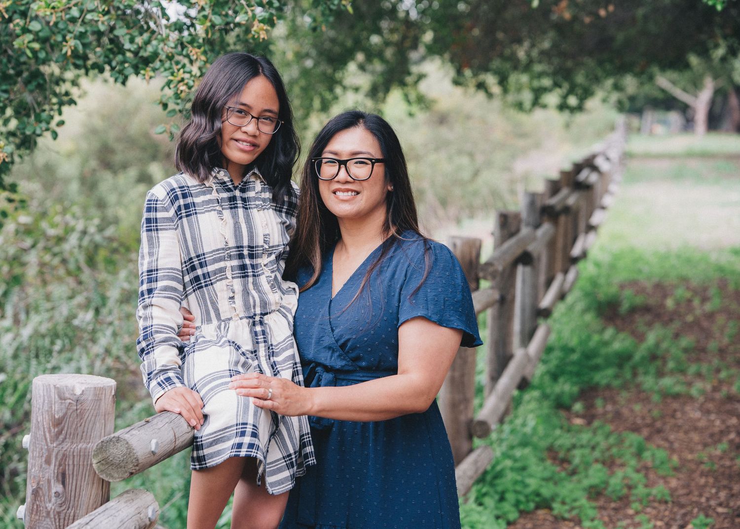 Two people in casual attire lean against a rustic wooden fence at a park during daytime.