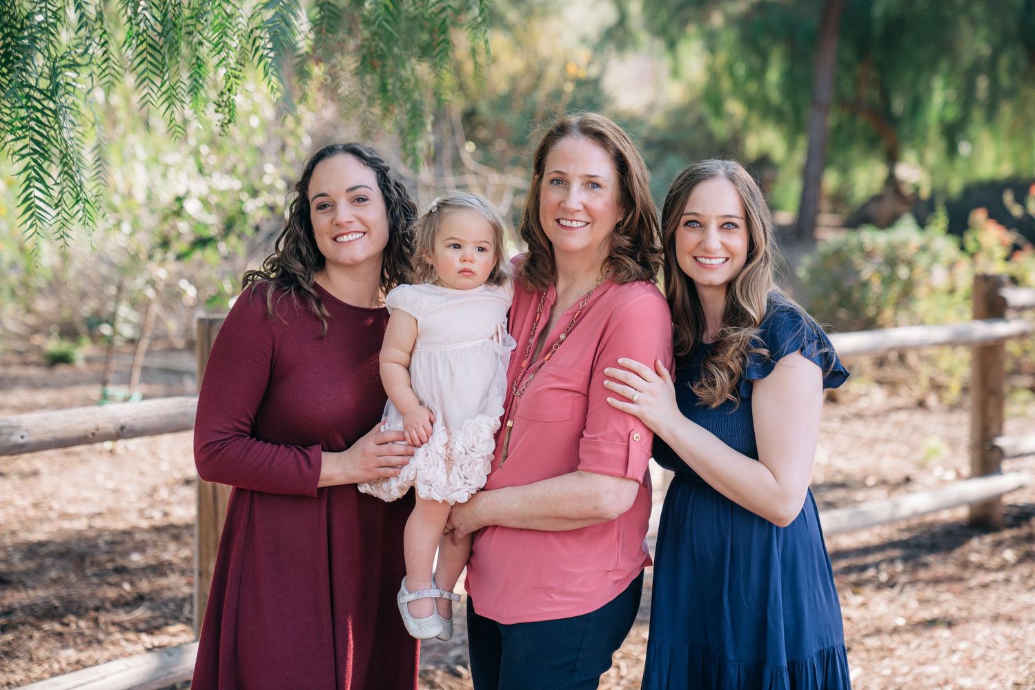 Outdoor family portrait in a park with wooden fence and greenery in the background.