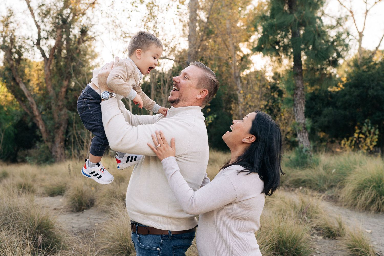 Family embraces joyfully during golden hour photoshoot in rustic outdoor setting with autumn trees and natural light.