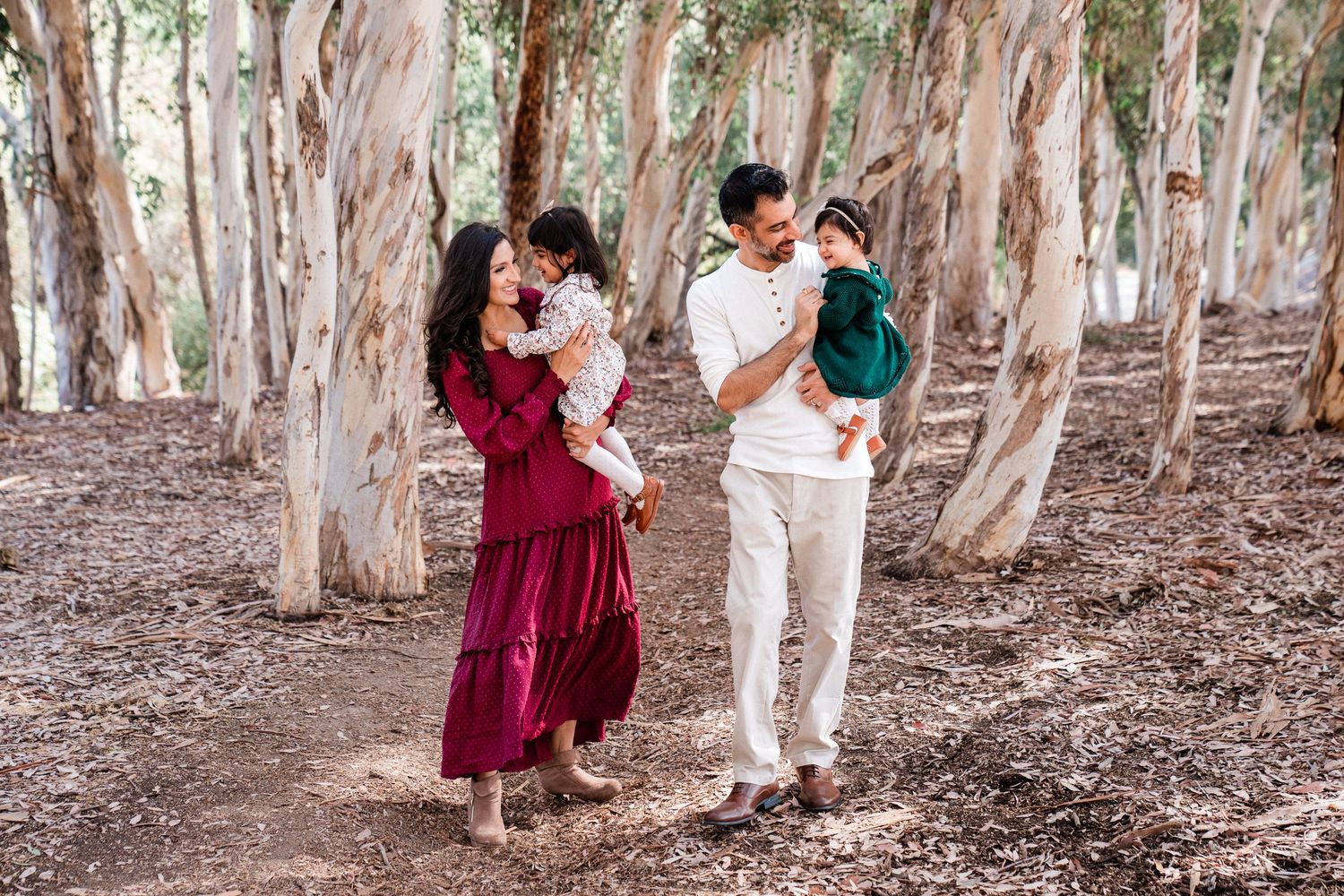 People in white and burgundy outfits pose together in a wooded grove of tall eucalyptus trees.