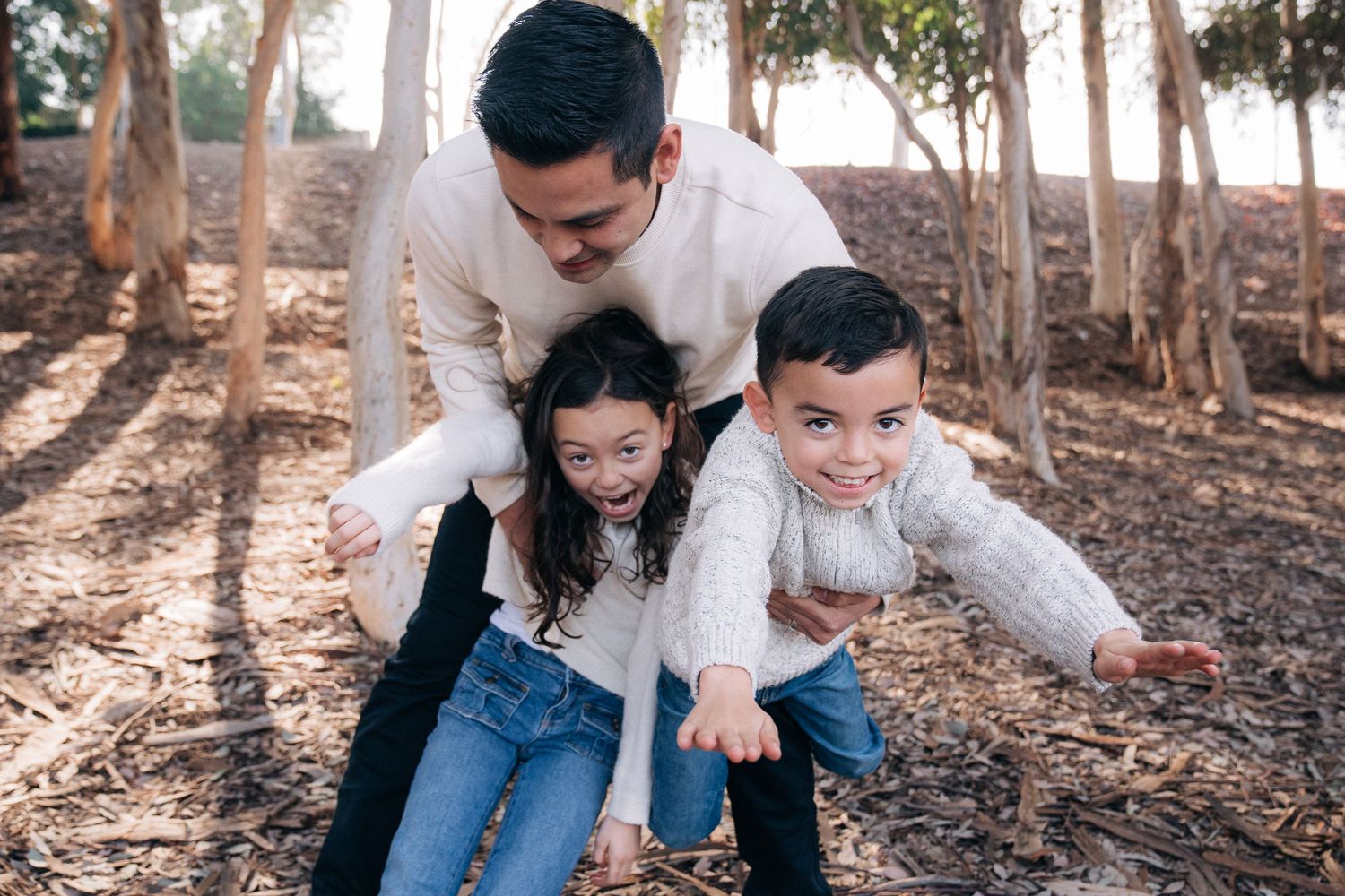 A candid family moment captured outdoors with sunlight filtering through trees in the background.