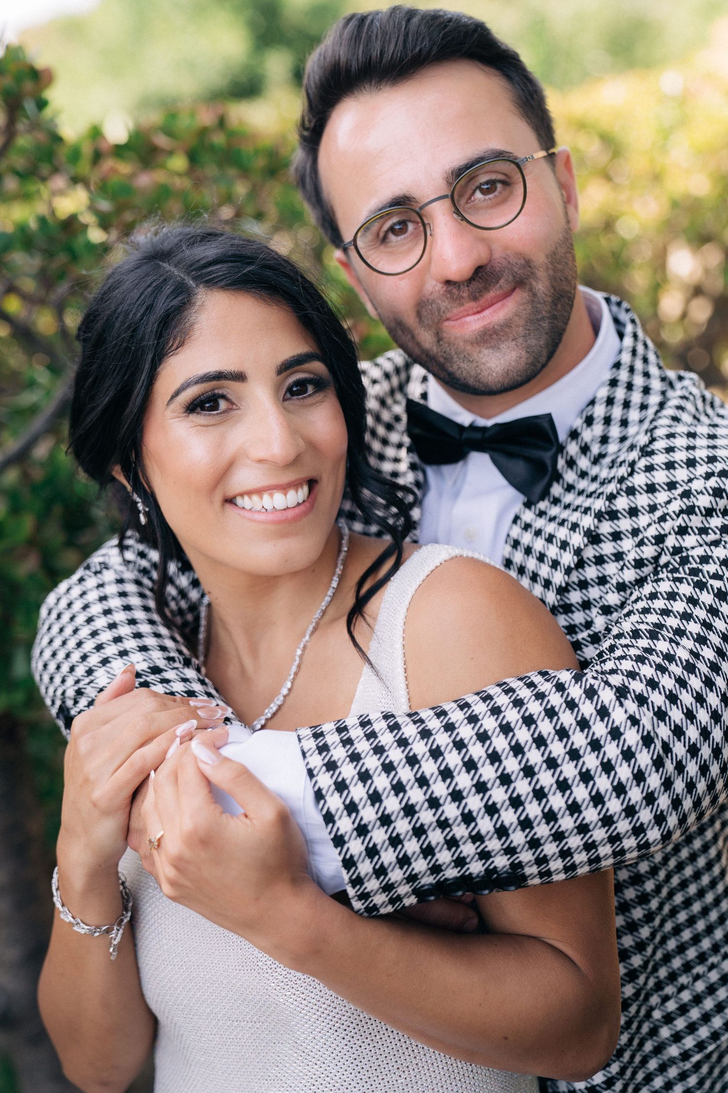 A couple shares a romantic embrace outdoors, wearing coordinating houndstooth patterns and formal attire.