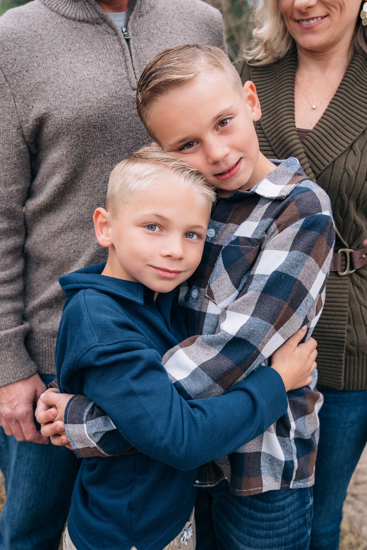 Siblings share warm embrace wearing blue and plaid clothing in heartfelt candid photo series.