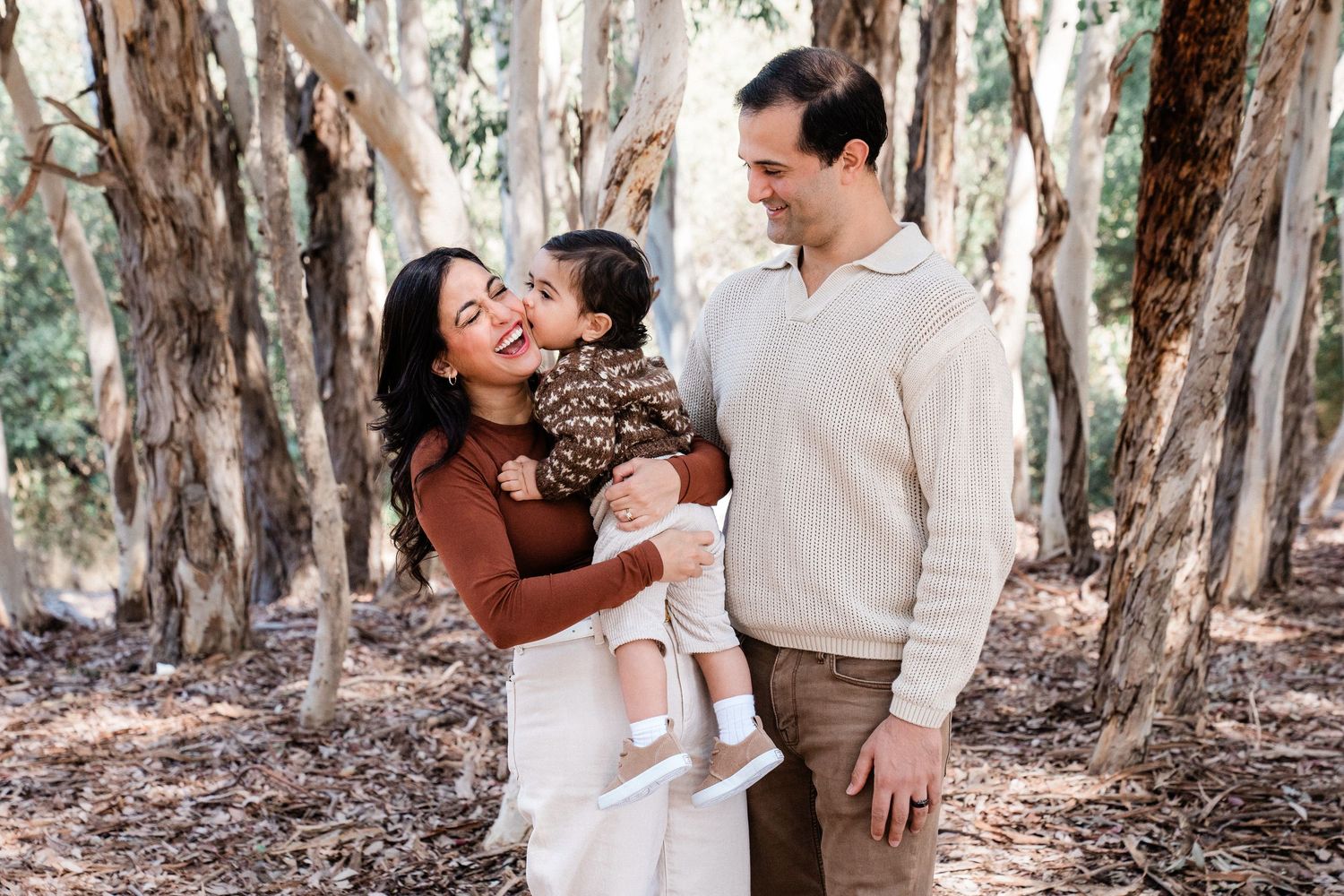 Romantic couple embraces in a sunlit eucalyptus grove during outdoor photo session.