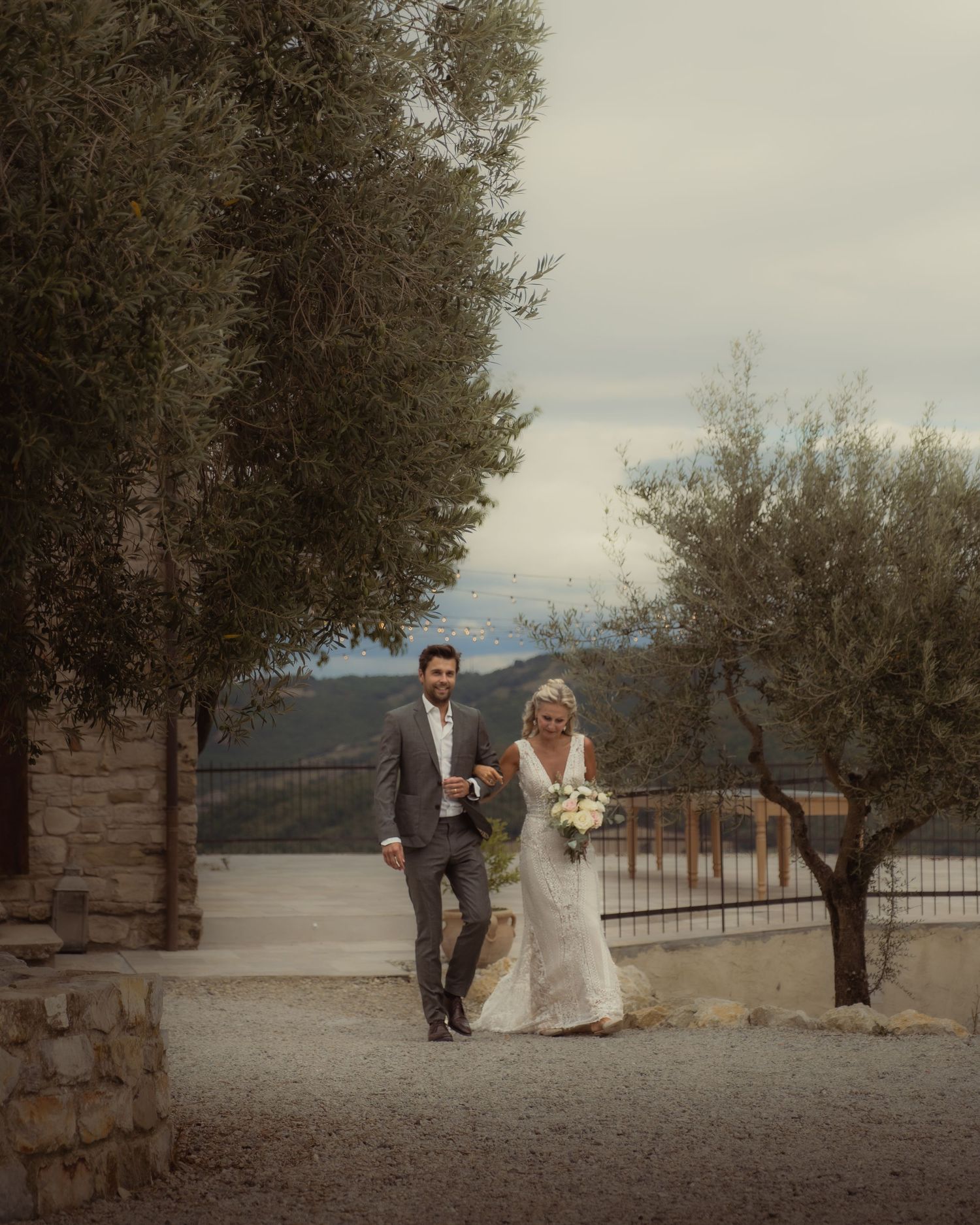 Couple walking along stone path surrounded by trees on their wedding day.