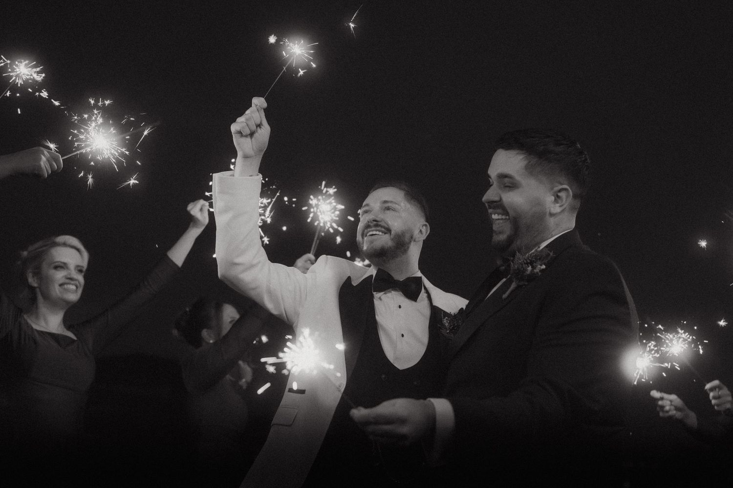 A celebratory moment captured in black and white with sparklers glowing against the night sky at an elegant event.