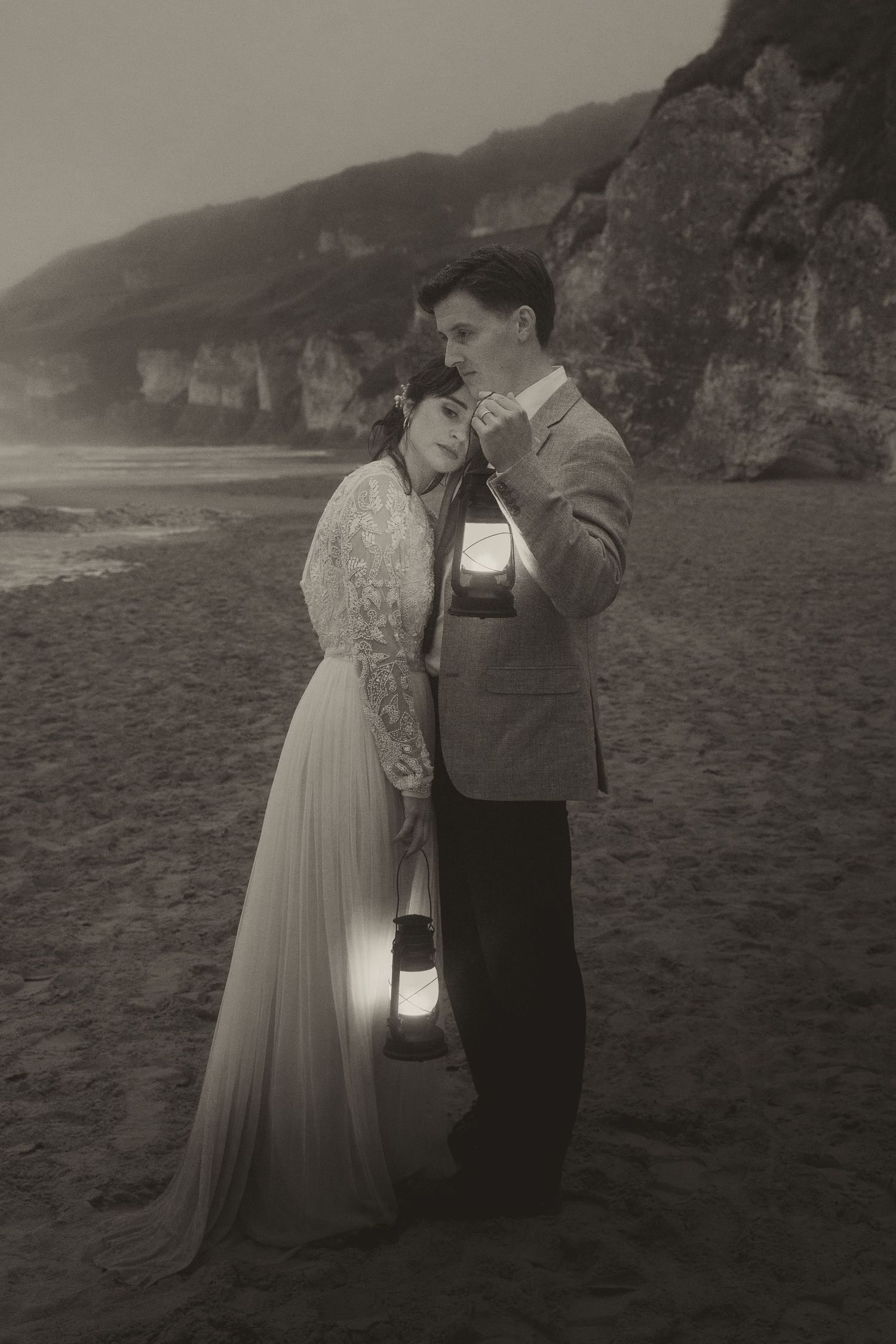 Vintage-style photo of couple with lanterns embracing on foggy beach.