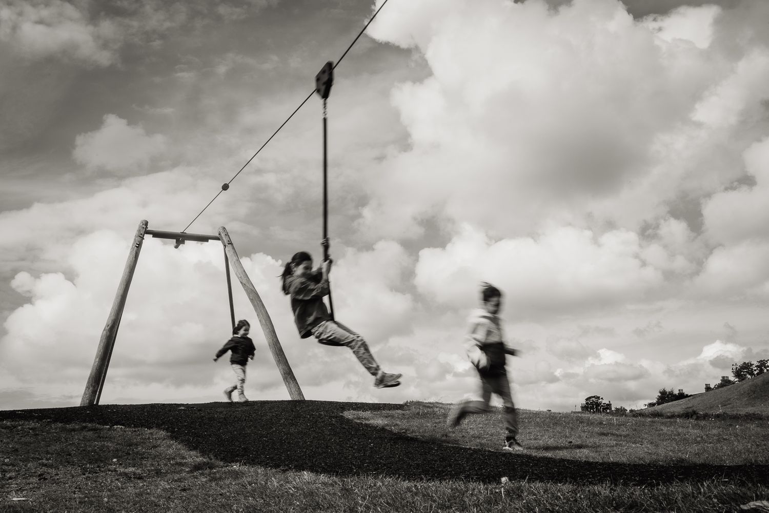 Three siblings playing on a zip wire in park in Fife