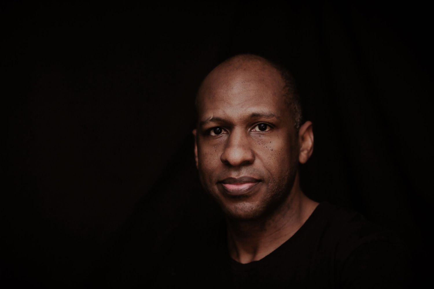 Dramatic portrait against black background in dark clothing.