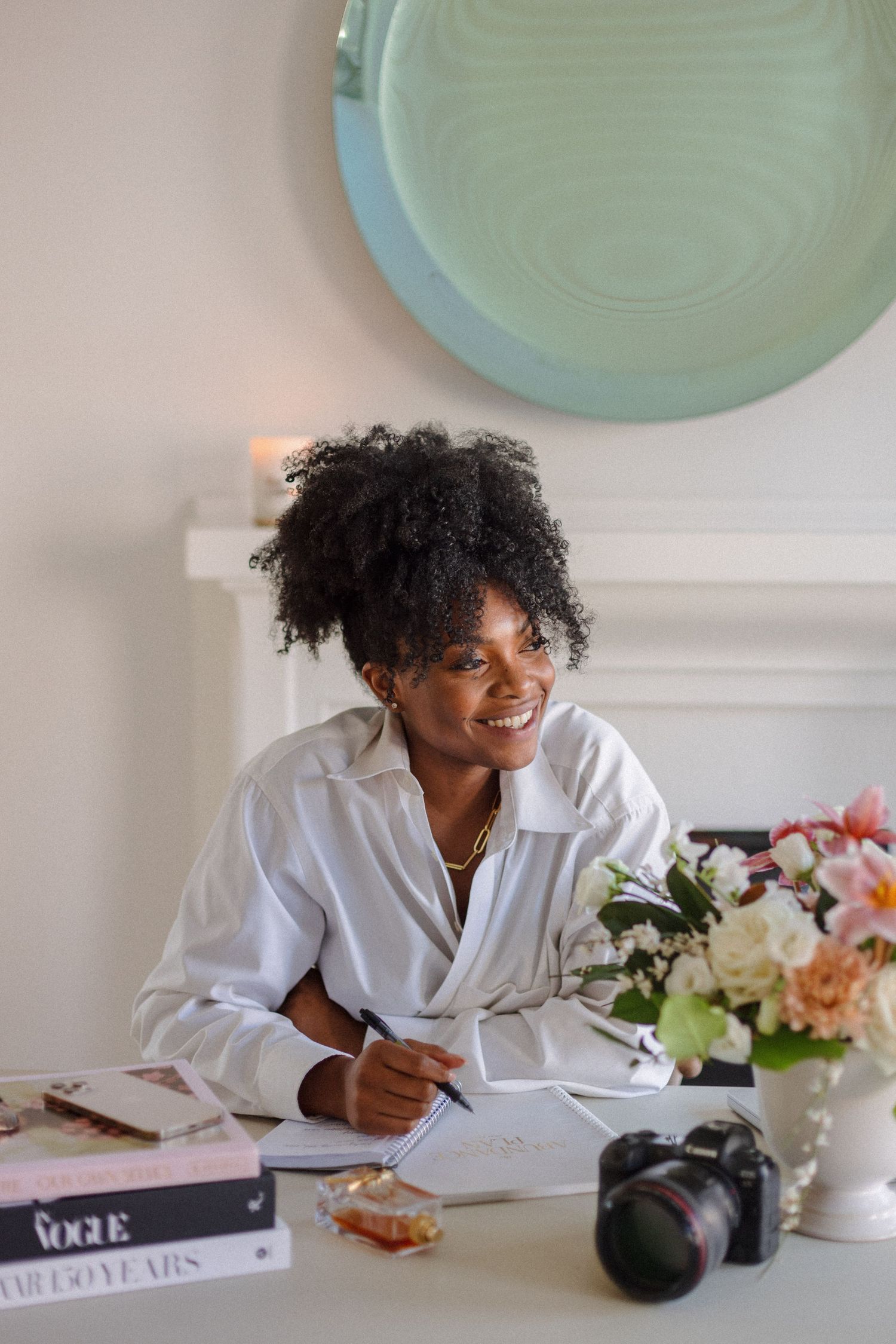 A content creator working at a stylish desk setup with flowers and photography equipment.
