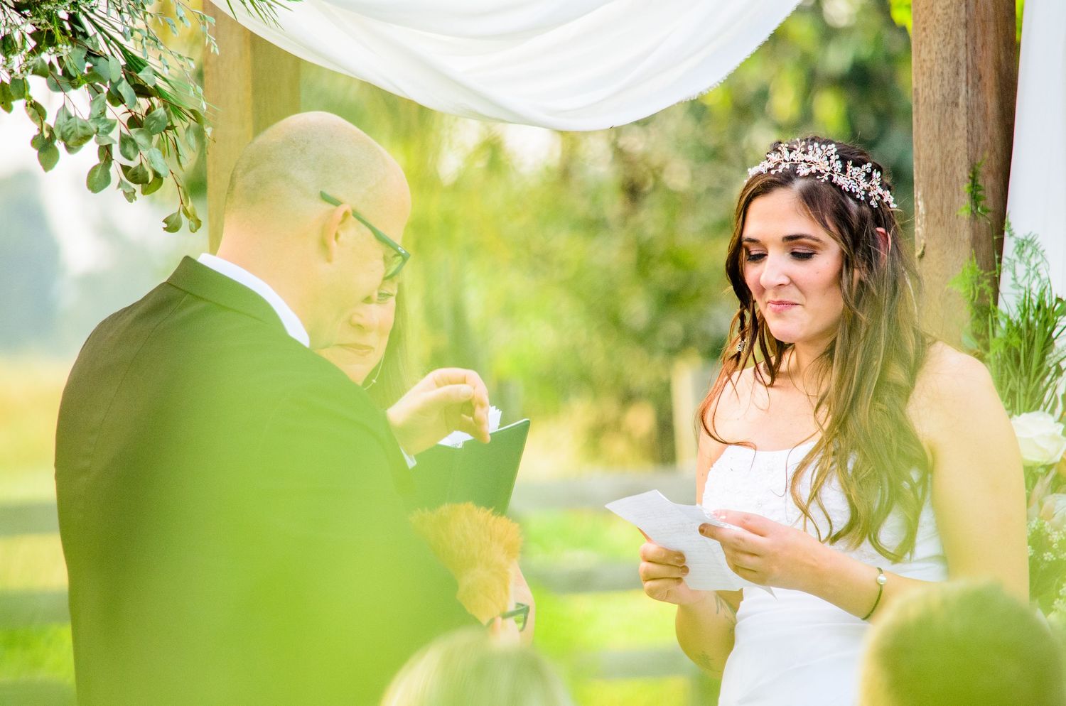 Outdoor wedding ceremony in garden setting with white fabric draping and natural greenery.