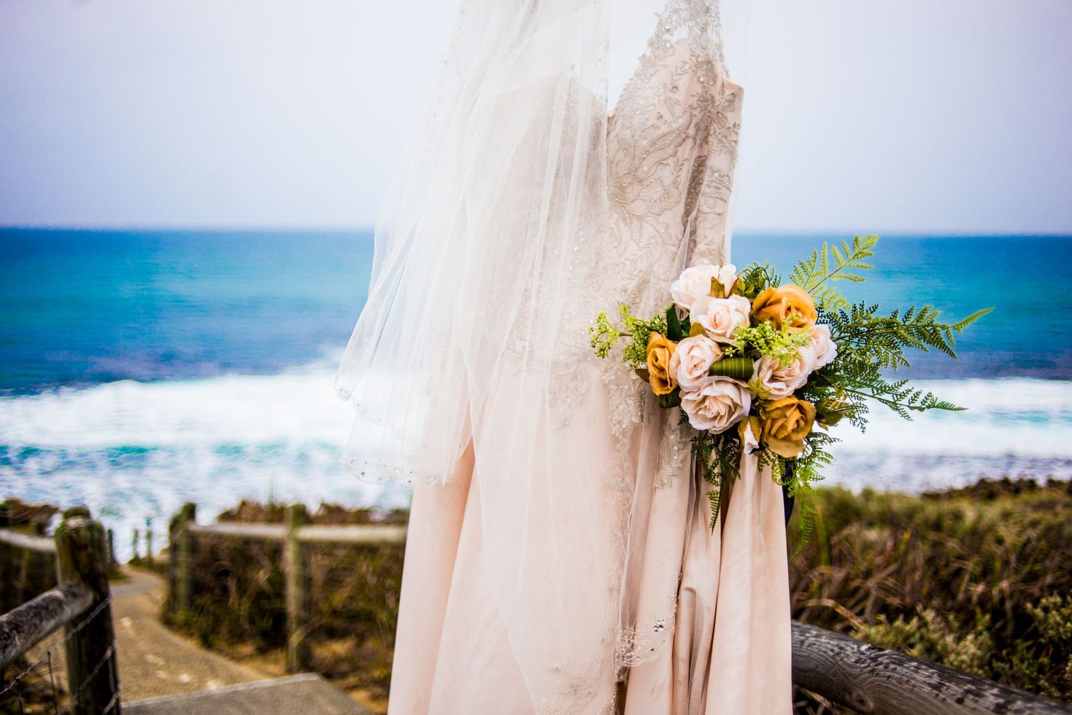 Elegant bridal bouquet with blush roses against ocean backdrop with veil details.