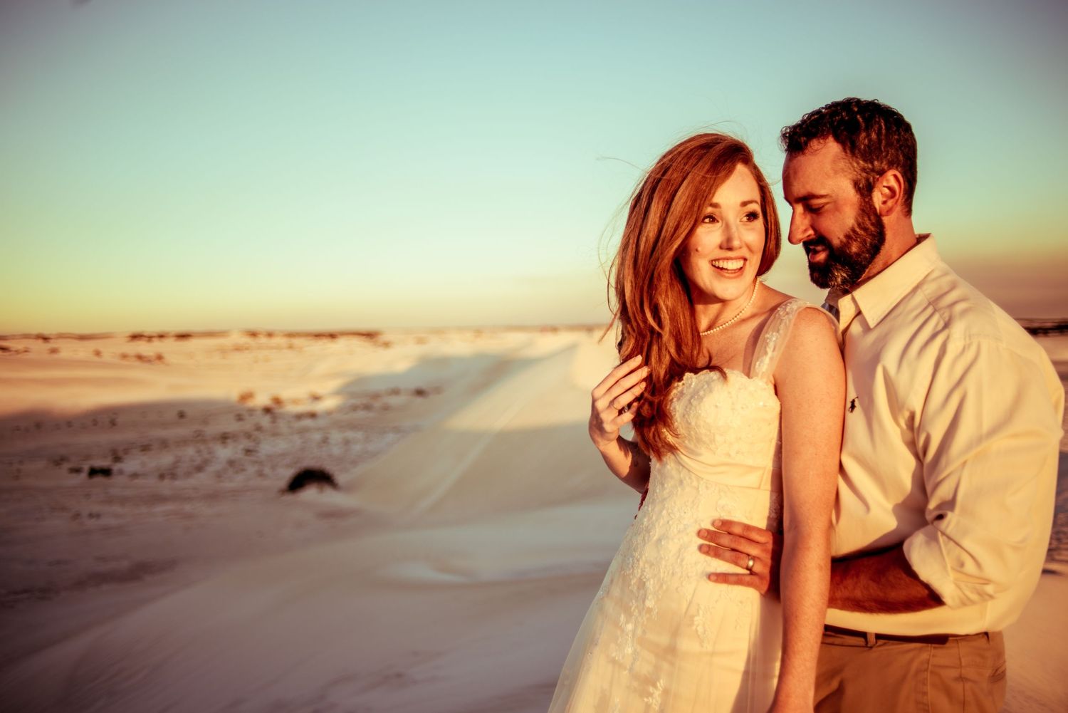 Romantic sunset beach portrait with couple in wedding attire against golden sky.
