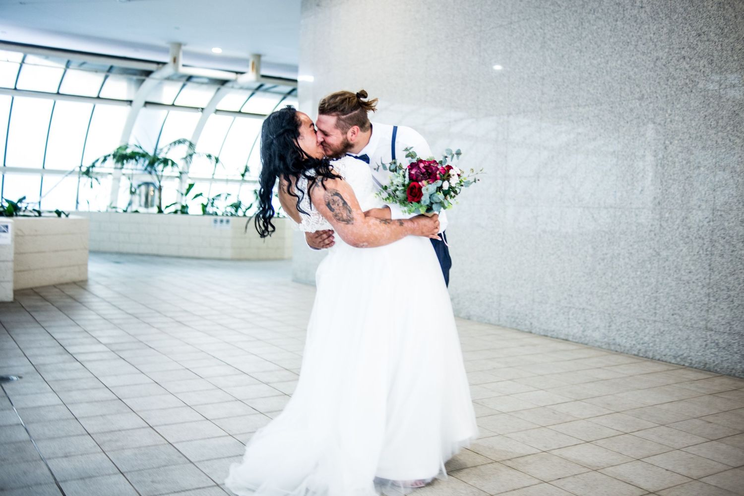 Wedding couple embracing and dancing in bright indoor venue with elegant white decor.