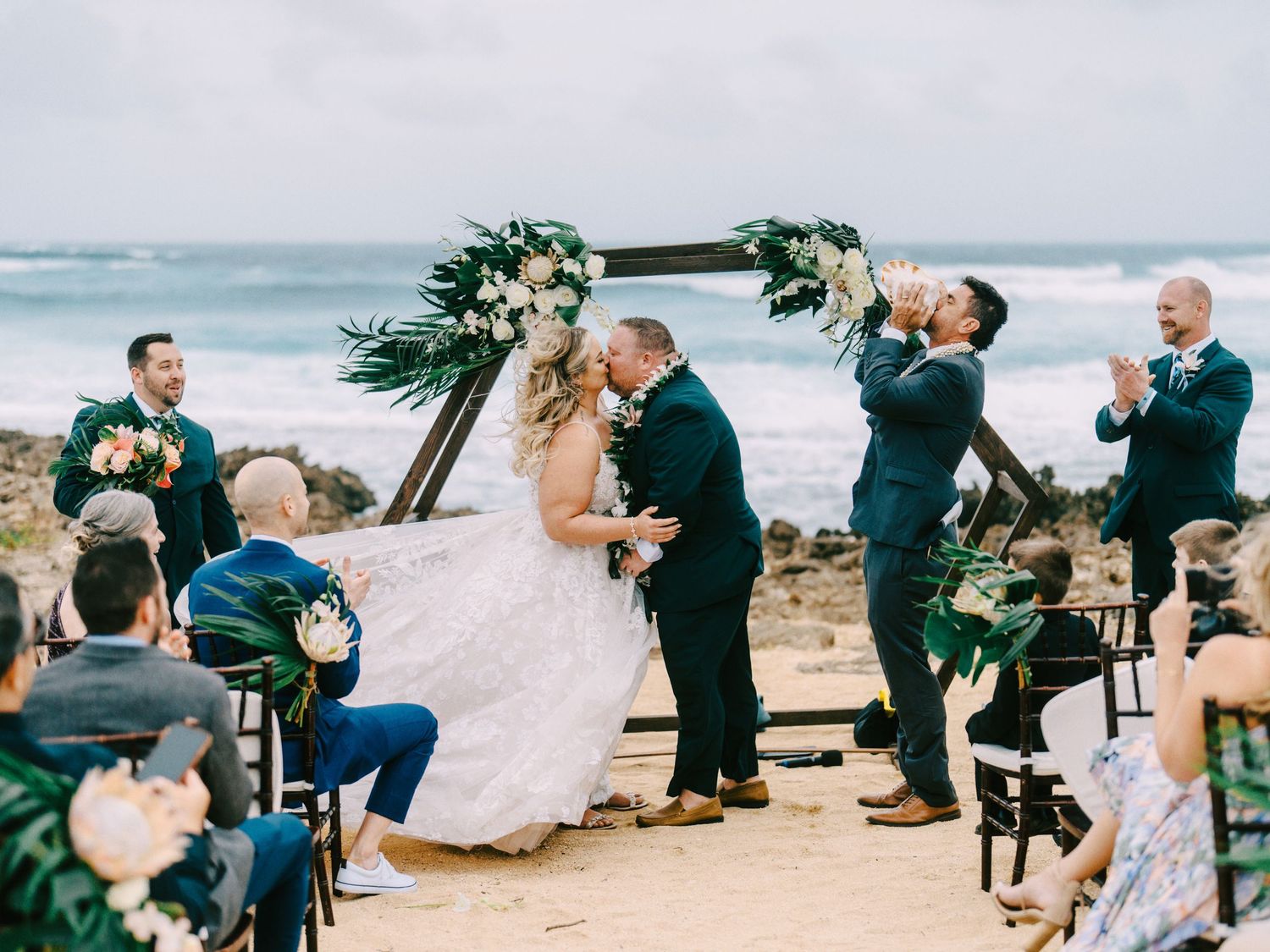 An intimate beach wedding ceremony setup with chairs and guests by the ocean.