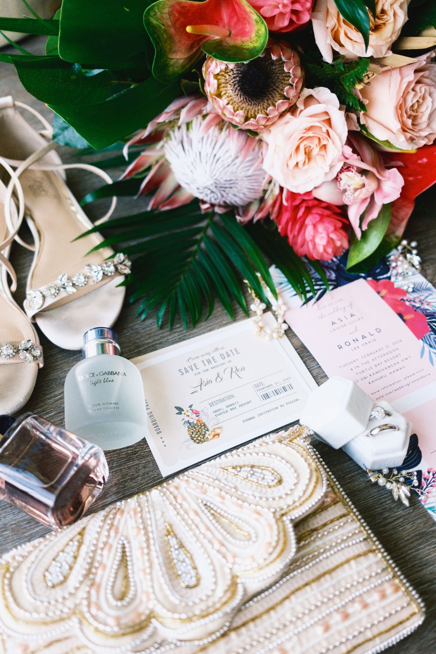 Wedding details flatlay with tropical flowers, invitations and pearl-embellished clutch.
