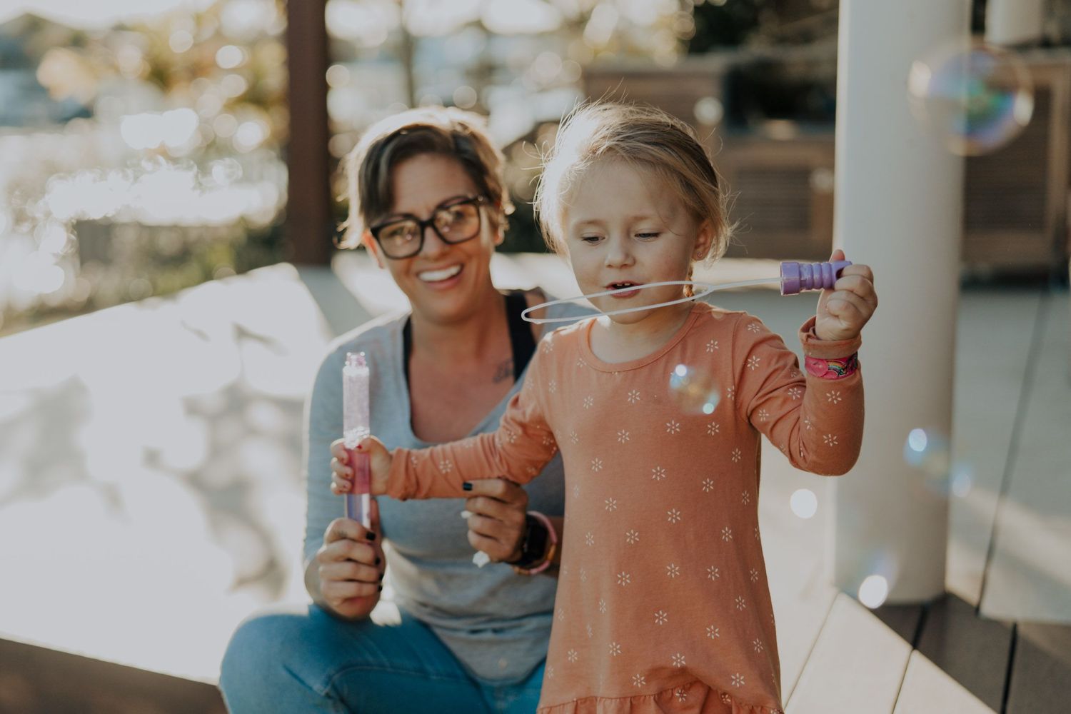 A mum and her child blowing bubbles in the backyard