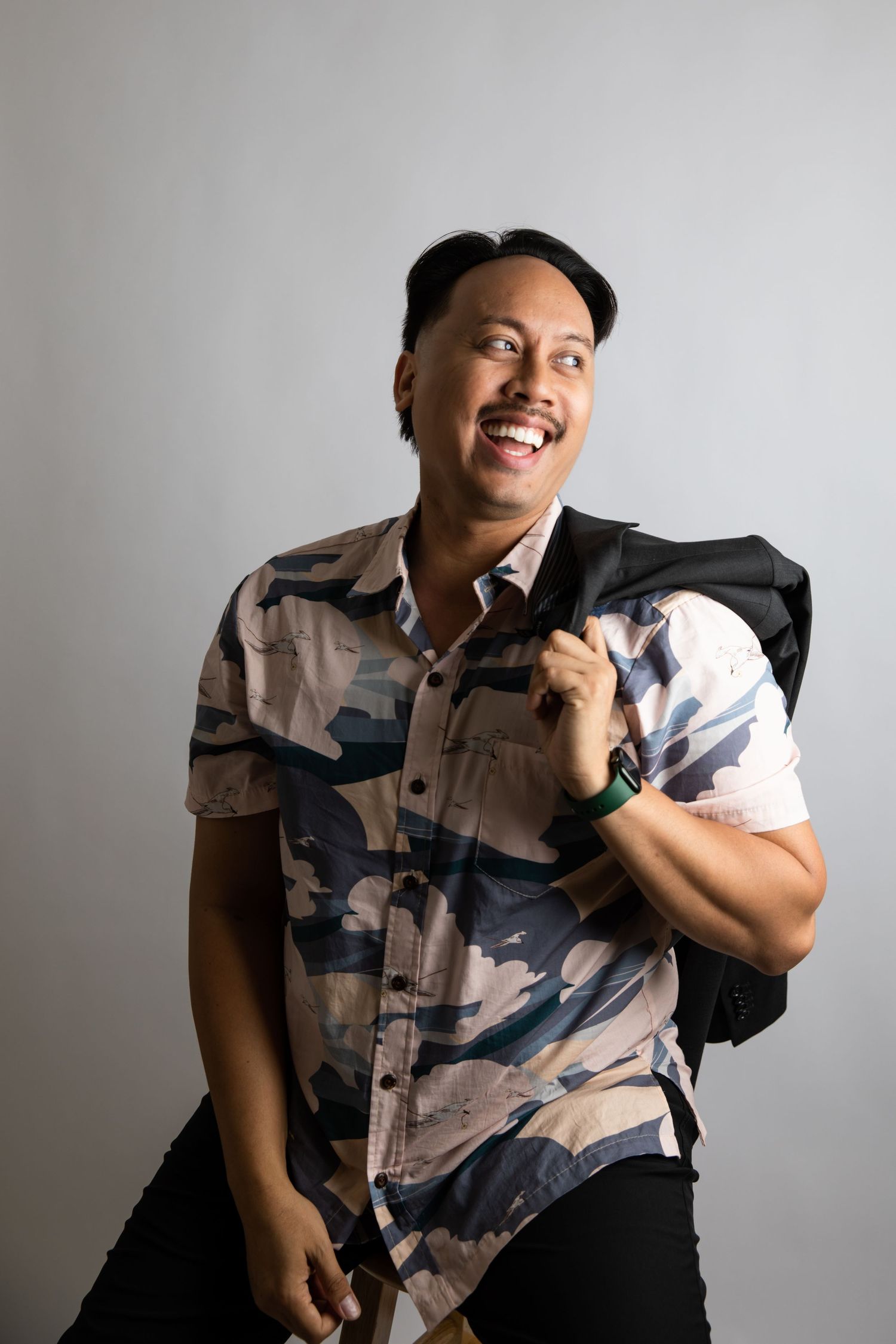 Casually dressed person in camo shirt smiling and posing against light gray background.