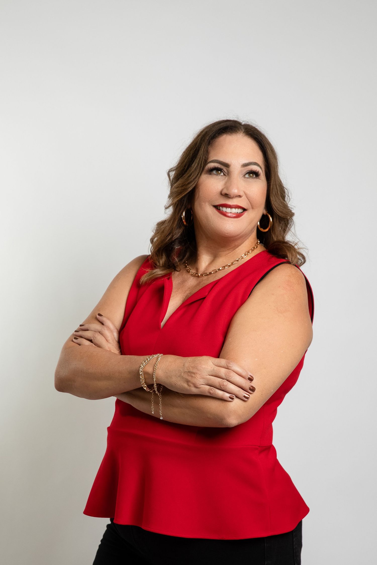 Woman in red sleeveless peplum top and black pants poses confidently against white background.