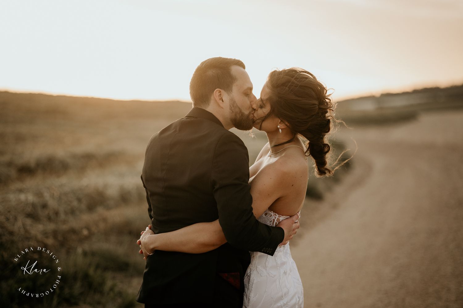 Newlyweds share an intimate moment at sunset on a dirt path in the countryside.