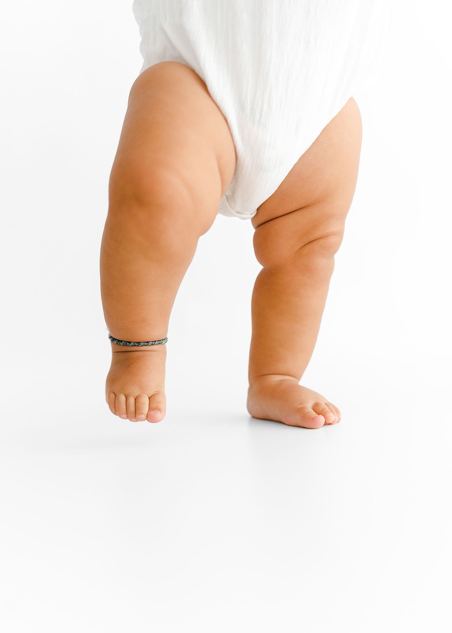 Close up view of chubby baby legs wearing a white outfit against white background.