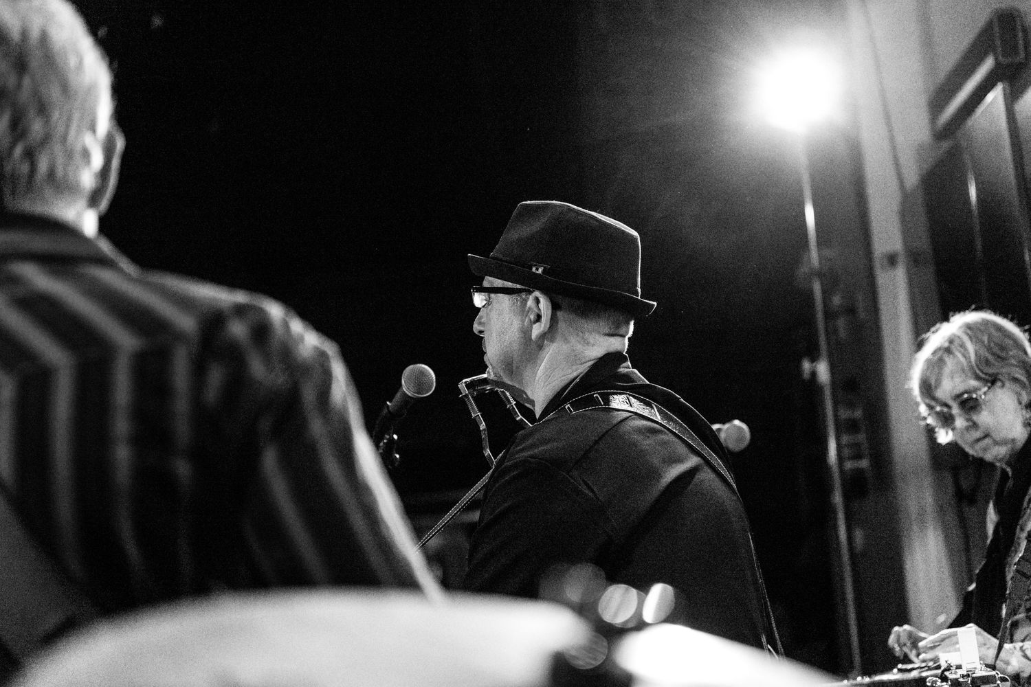 Black and white image of three people on a stage, light coming from upper right corner