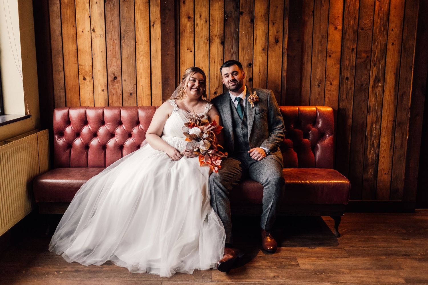 A wedding portrait featuring traditional attire against rustic wooden paneling and red leather seating.