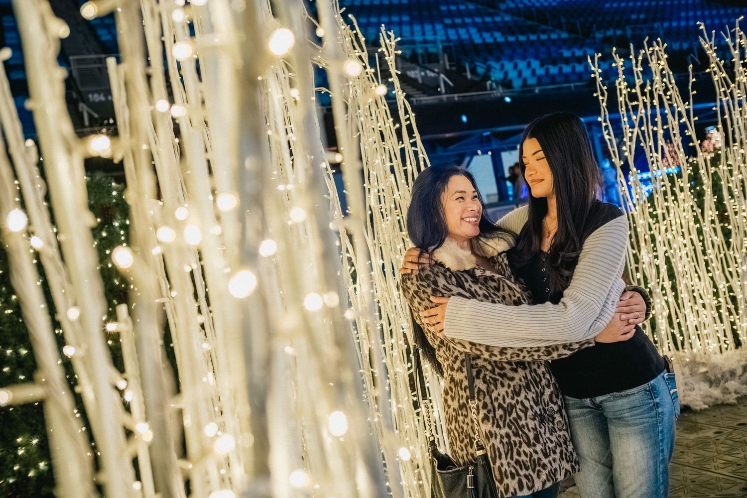 People embracing amid sparkling light installations at an outdoor evening event.