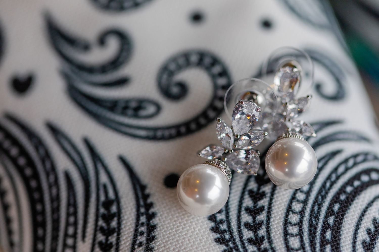 Close-up of delicate pearl and crystal wedding jewelry on patterned fabric.