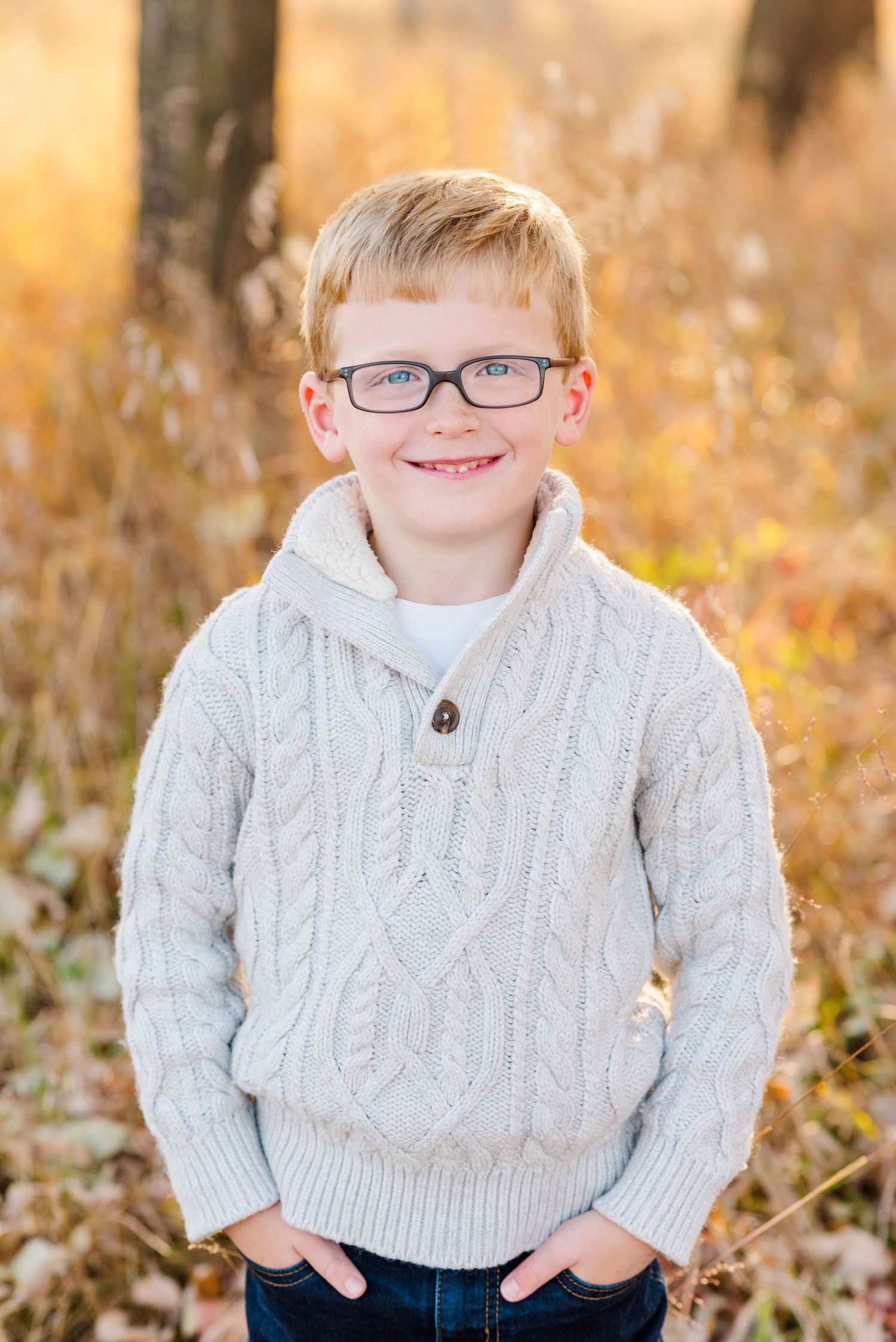 Portrait of a child in a white cable knit sweater against an autumn background.