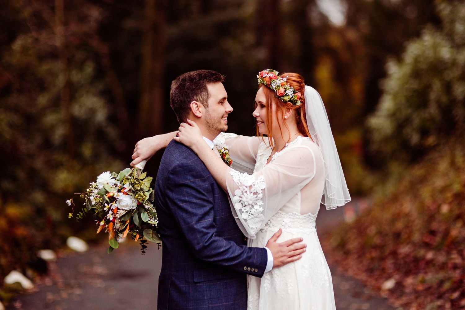 A romantic autumn wedding portrait with the couple embracing on a wooded path.