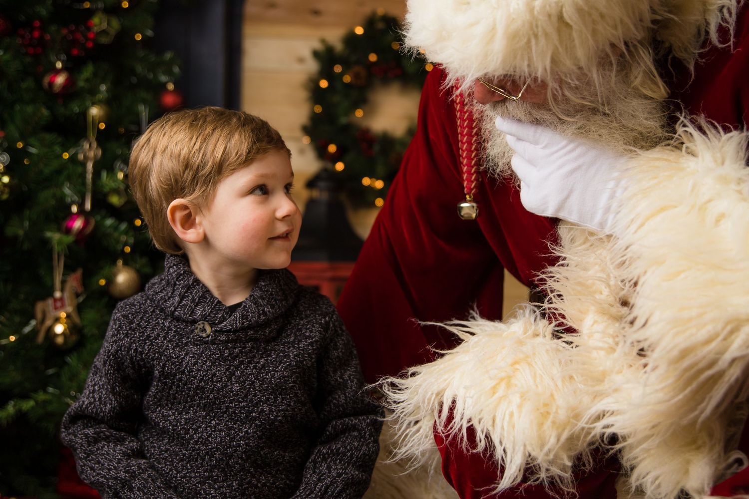 Young child gazing up at Santa Claus by decorated Christmas tree.