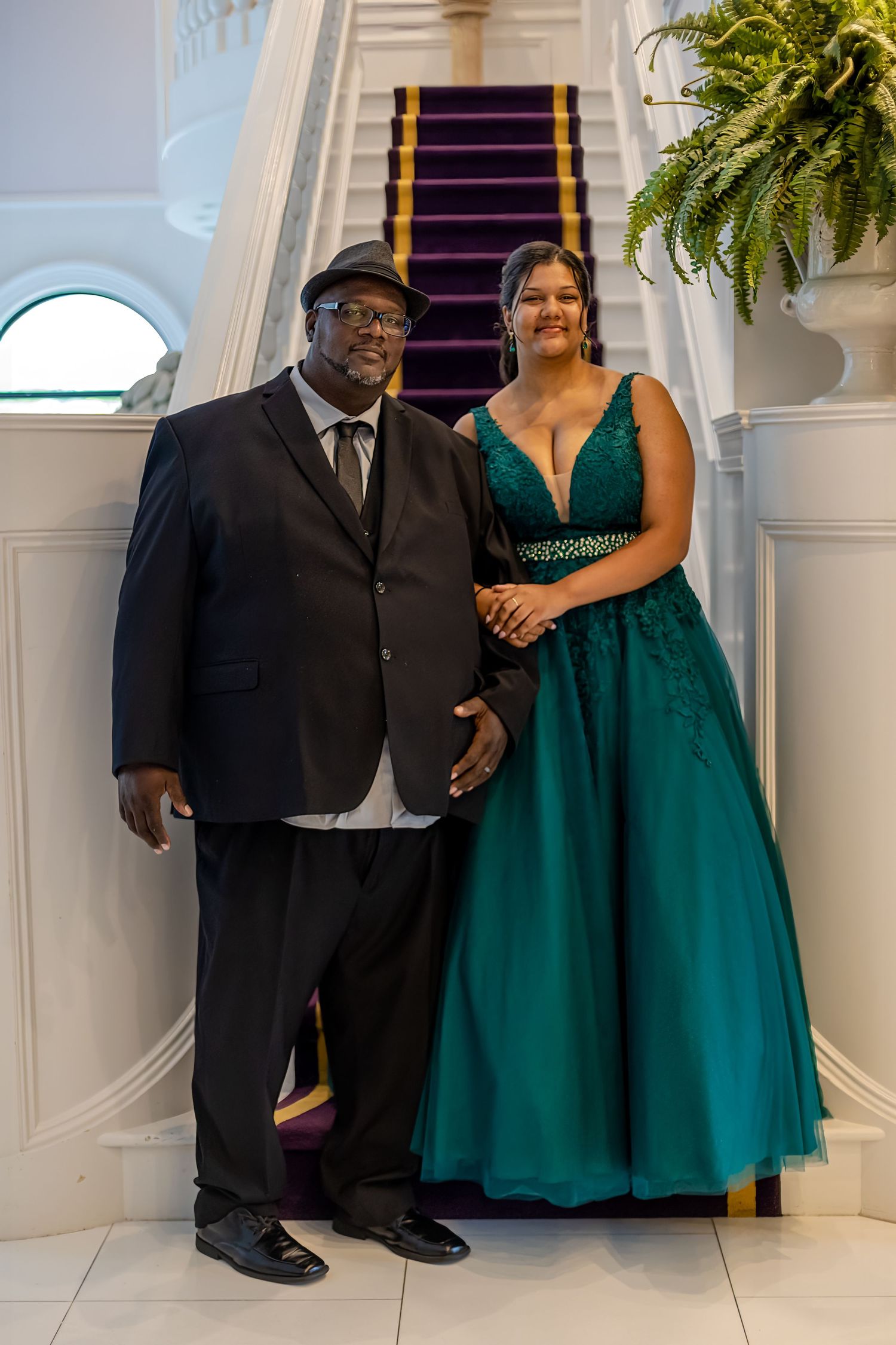 Formal event photo showing elegant emerald dress against white architectural backdrop.