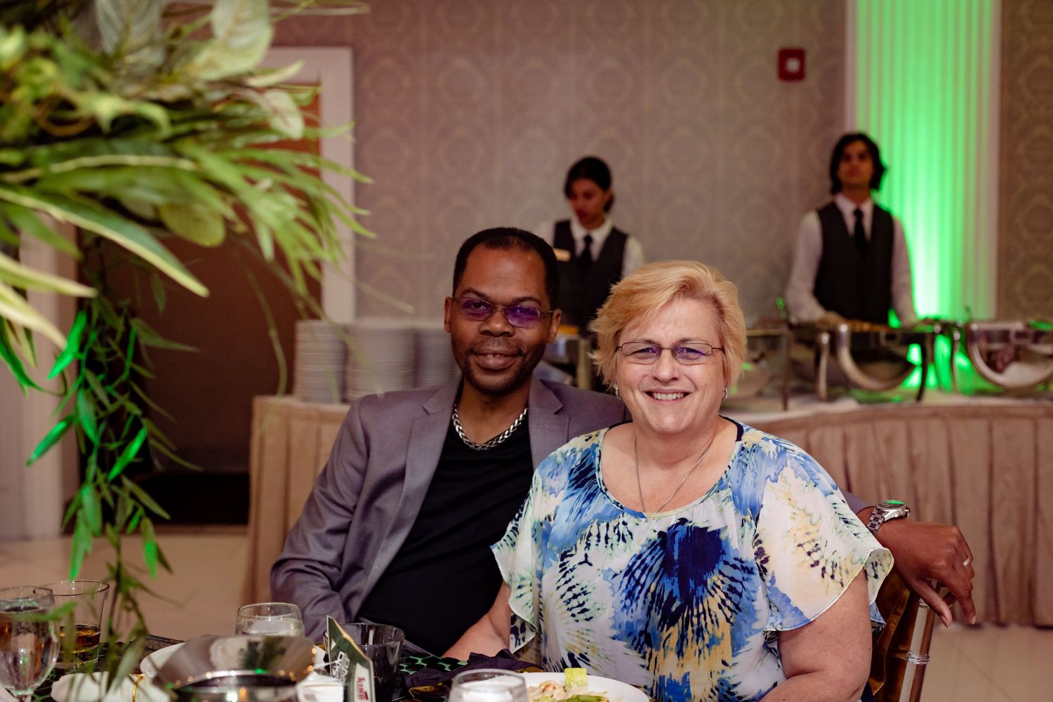 Wedding party gathers near elegant teal curtains and floral arrangements at a reception venue.