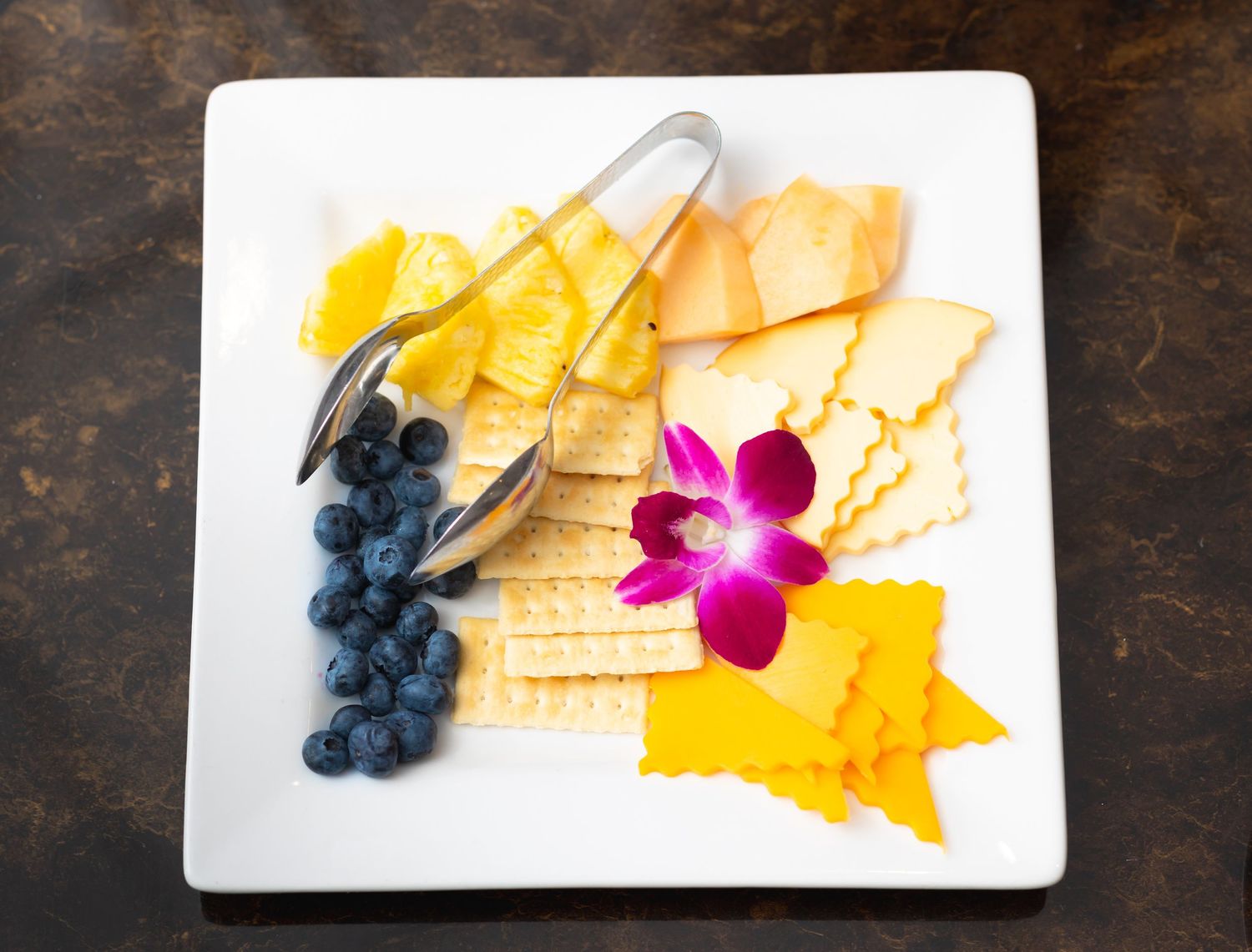 Artfully plated dessert with blueberries, yellow sauce and pink flower garnish.