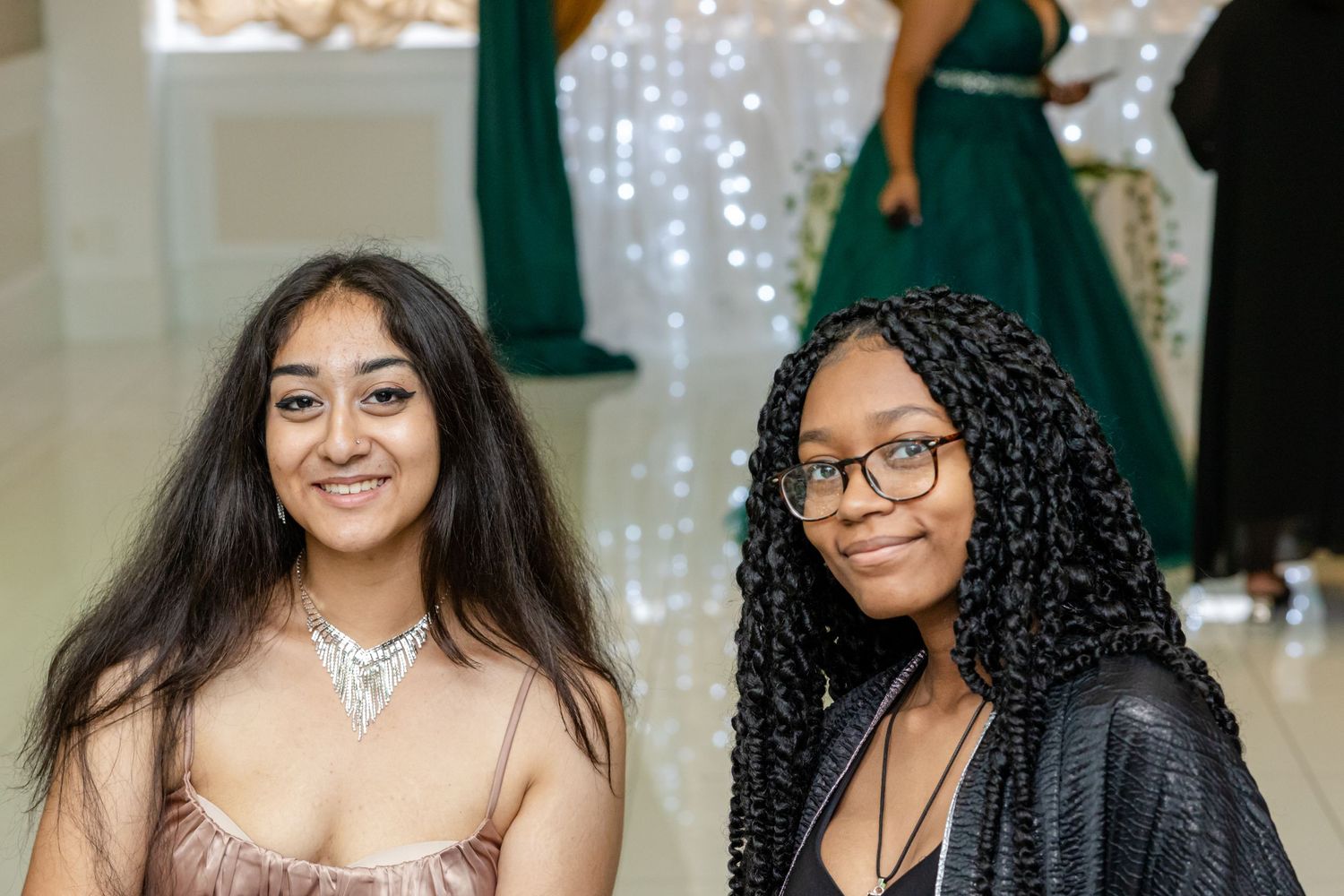 Celebration guests in emerald green and formal attire posing together at an elegant event with sparkling lights.