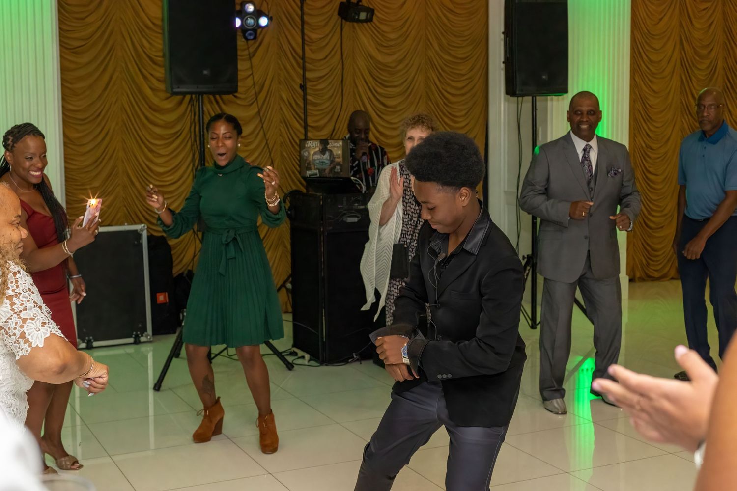 Dance floor surrounded by green uplighting at an indoor celebration venue.