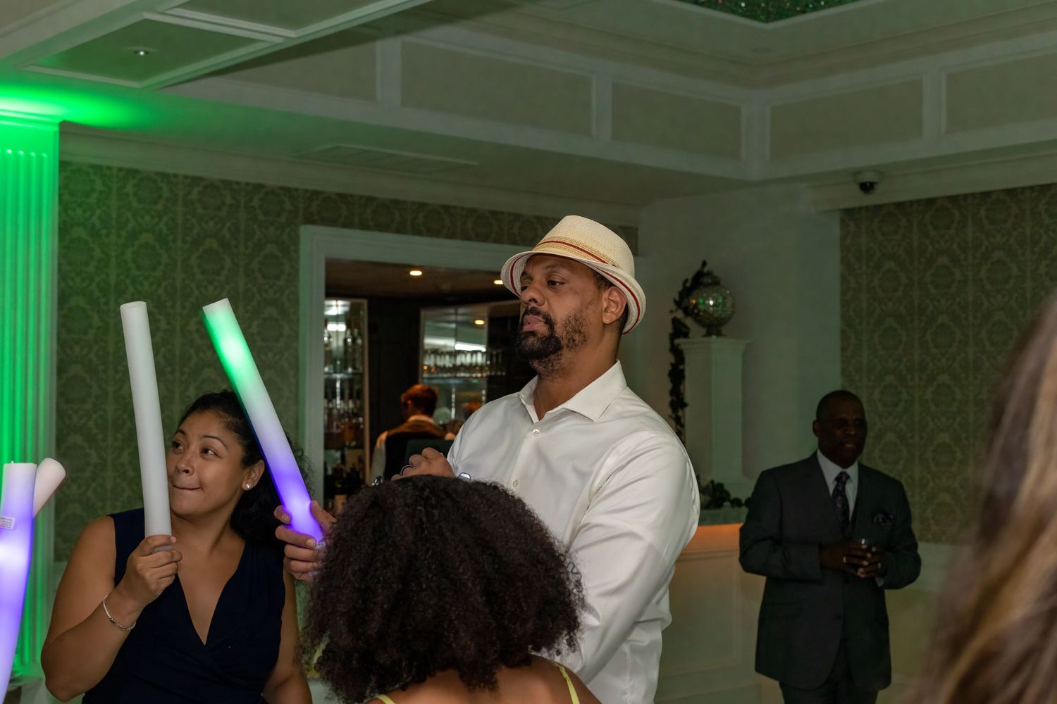 Party guests dancing and enjoying themselves at an indoor event with green accent lighting.