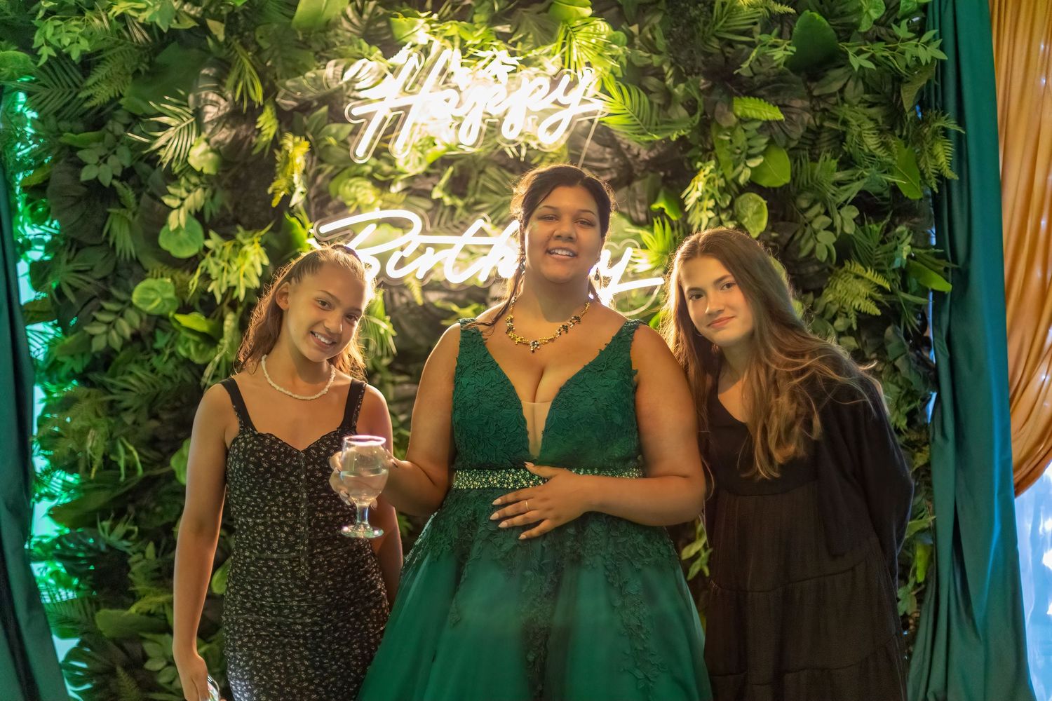 Wedding celebration in an elegant venue with green uplighting and decorative foliage on the walls.