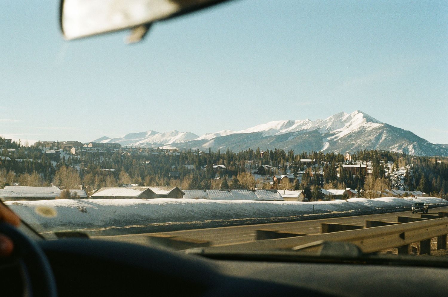 Panoramic winter landscape showing snow-capped mountains and an airfield under clear blue skies.