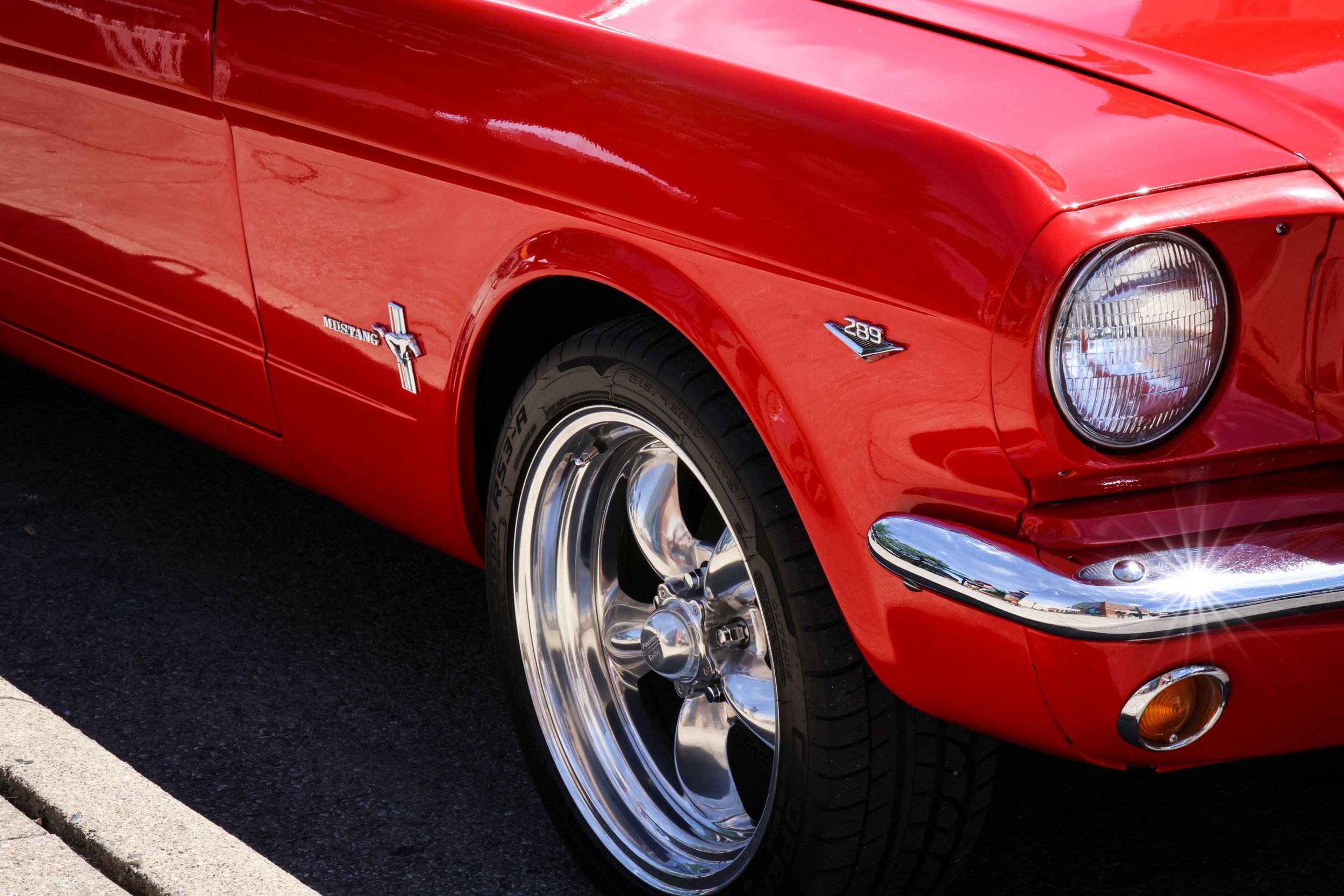 Front quarter panel detail of a red classic Ford Mustang with chrome wheel.