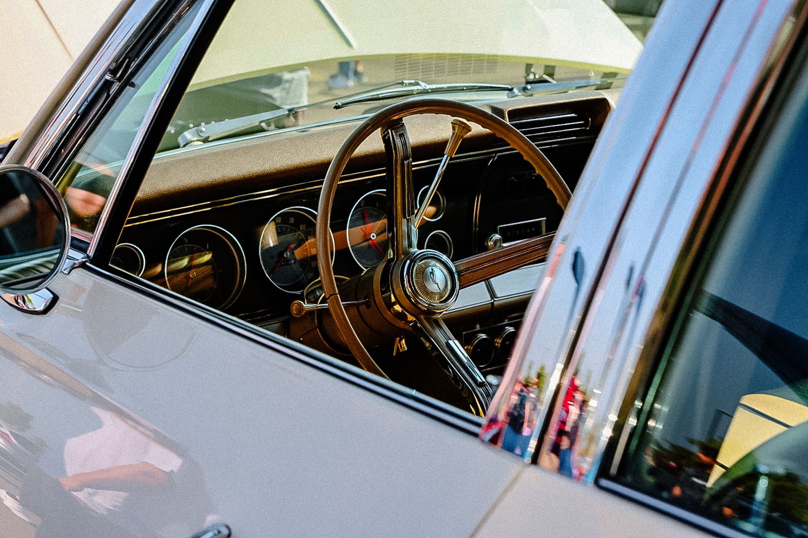 View through car window showing vintage wooden steering wheel and classic dashboard gauges in luxury automobile interior.