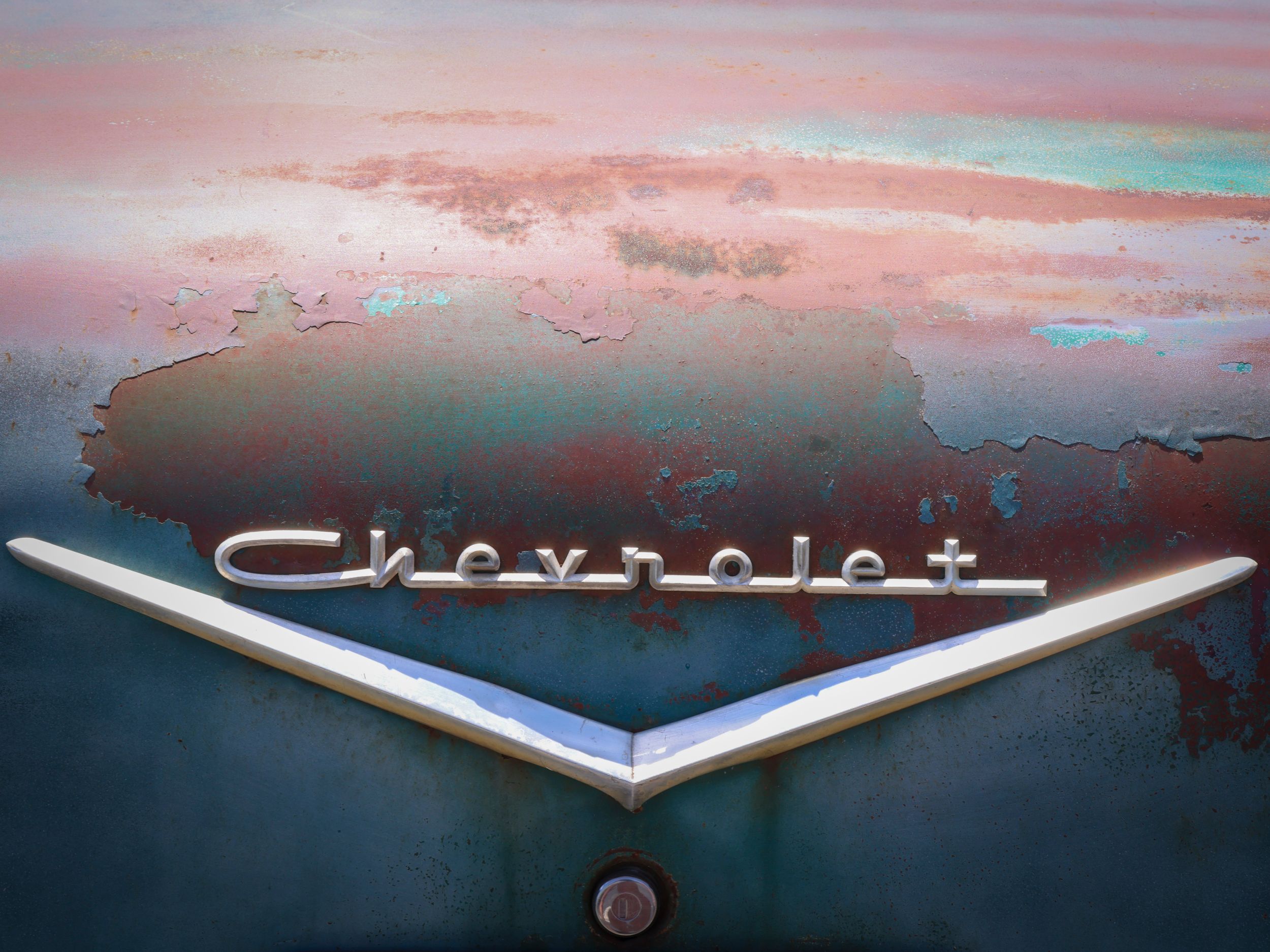 Close up of vintage Chevrolet emblem on weathered turquoise paint.