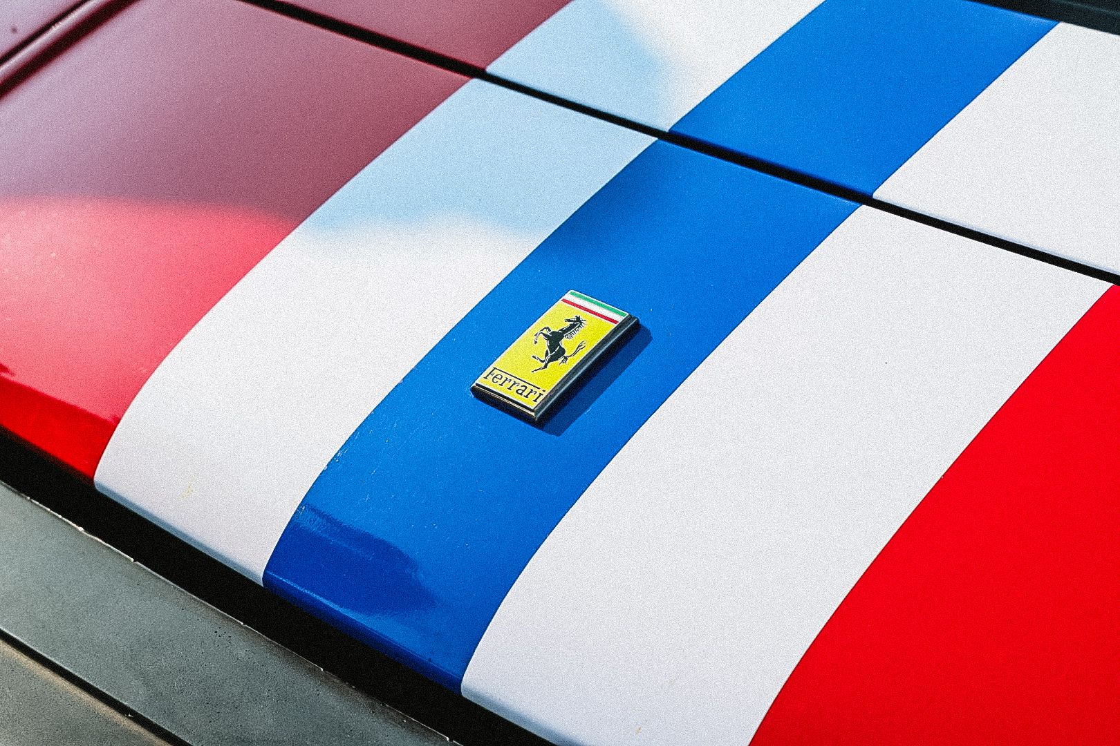 Ferrari logo badge on red and white striped car hood with blue racing stripe.