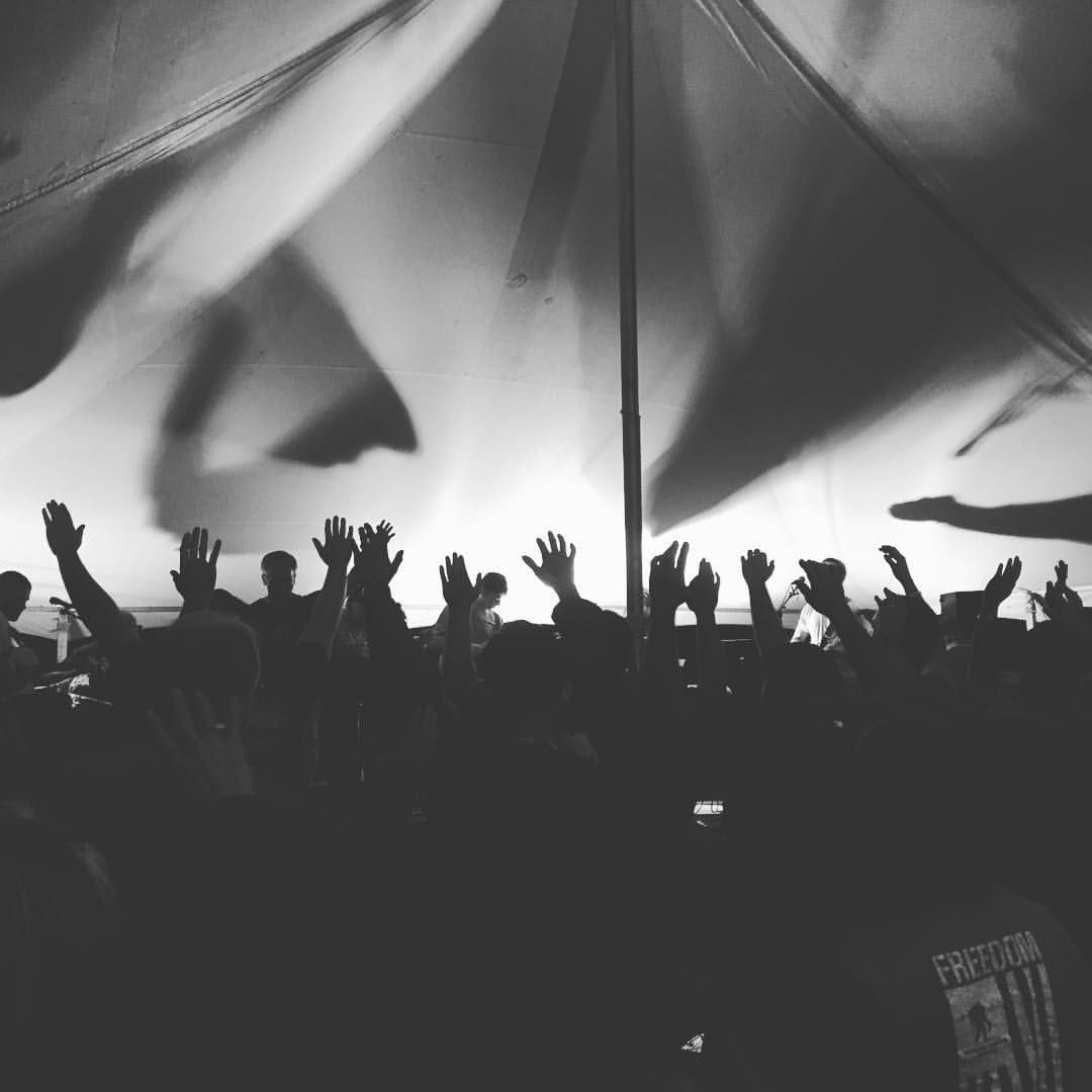Silhouetted crowd raises hands under tent canopy at concert or festival in black and white.