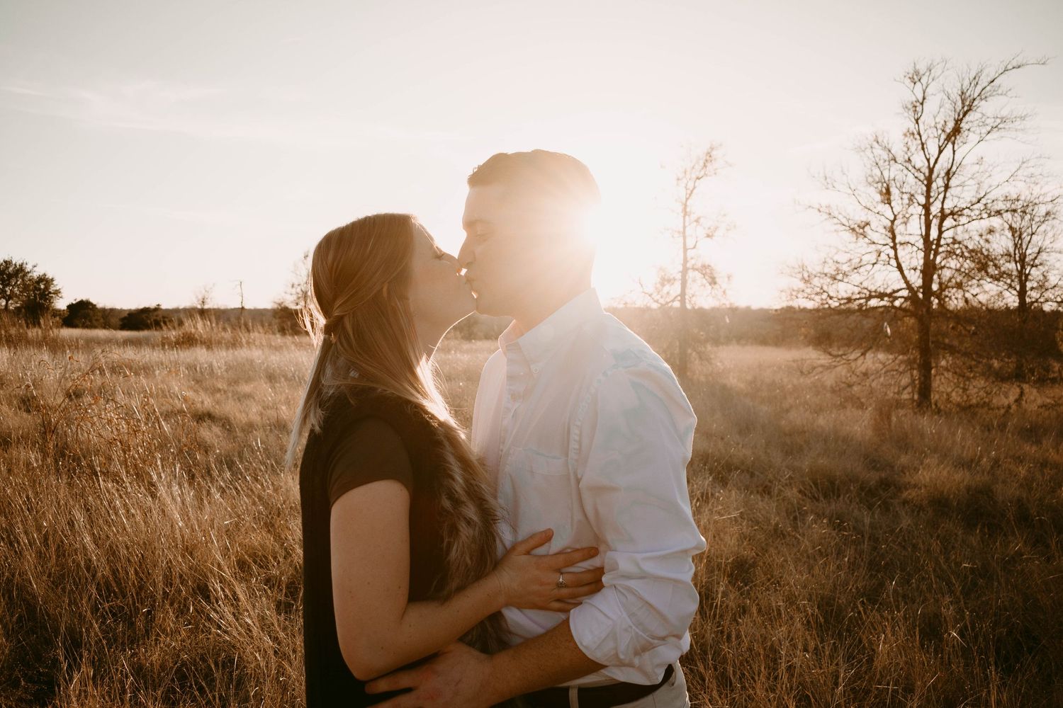 Silhouetted couple sharing tender moment in golden hour light amidst tall grass.