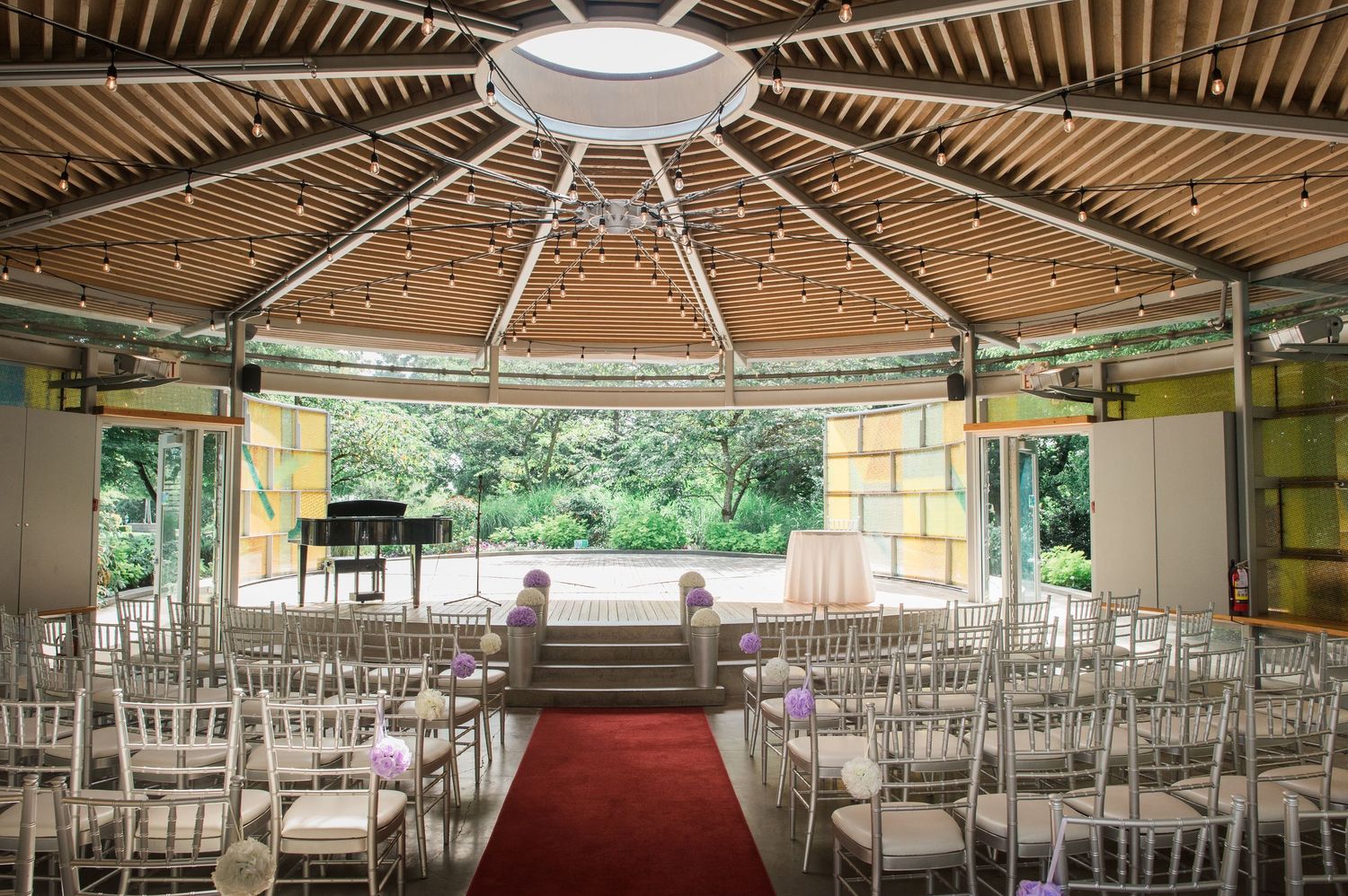 An indoor wedding ceremony space with wooden ceiling beams, white chairs, and red carpet aisle.